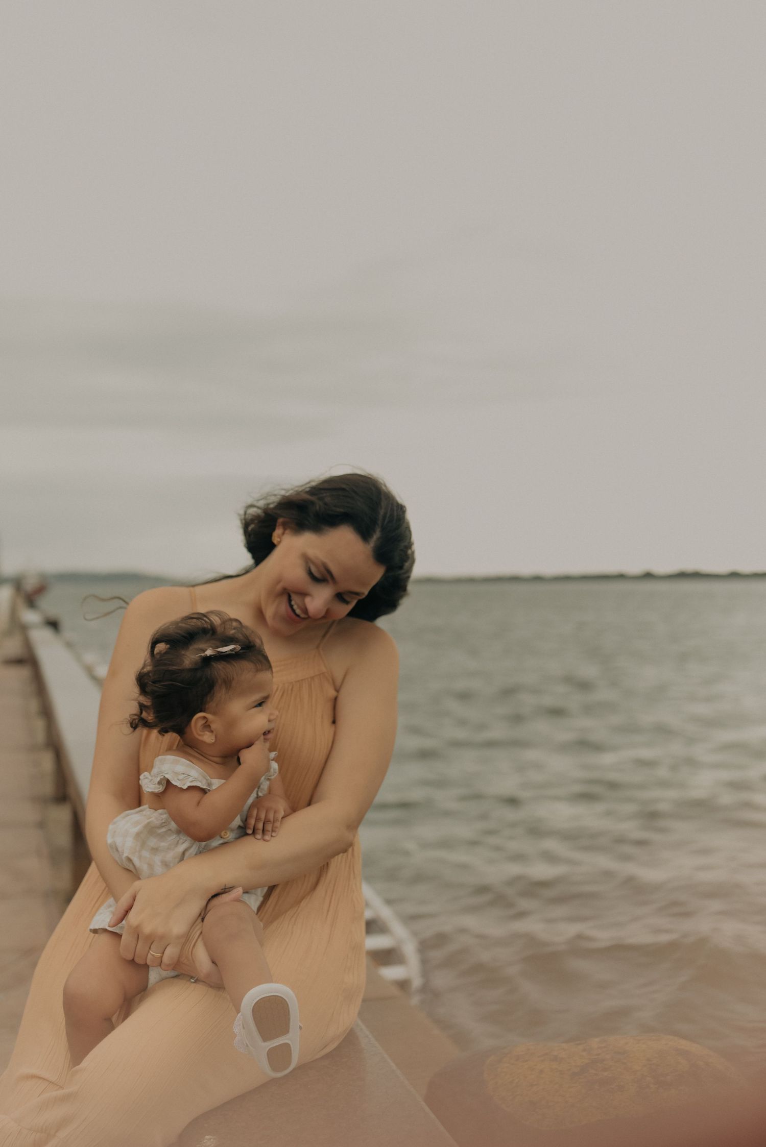 Parent and child share a joyful moment together by the water's edge wearing matching beige outfits.