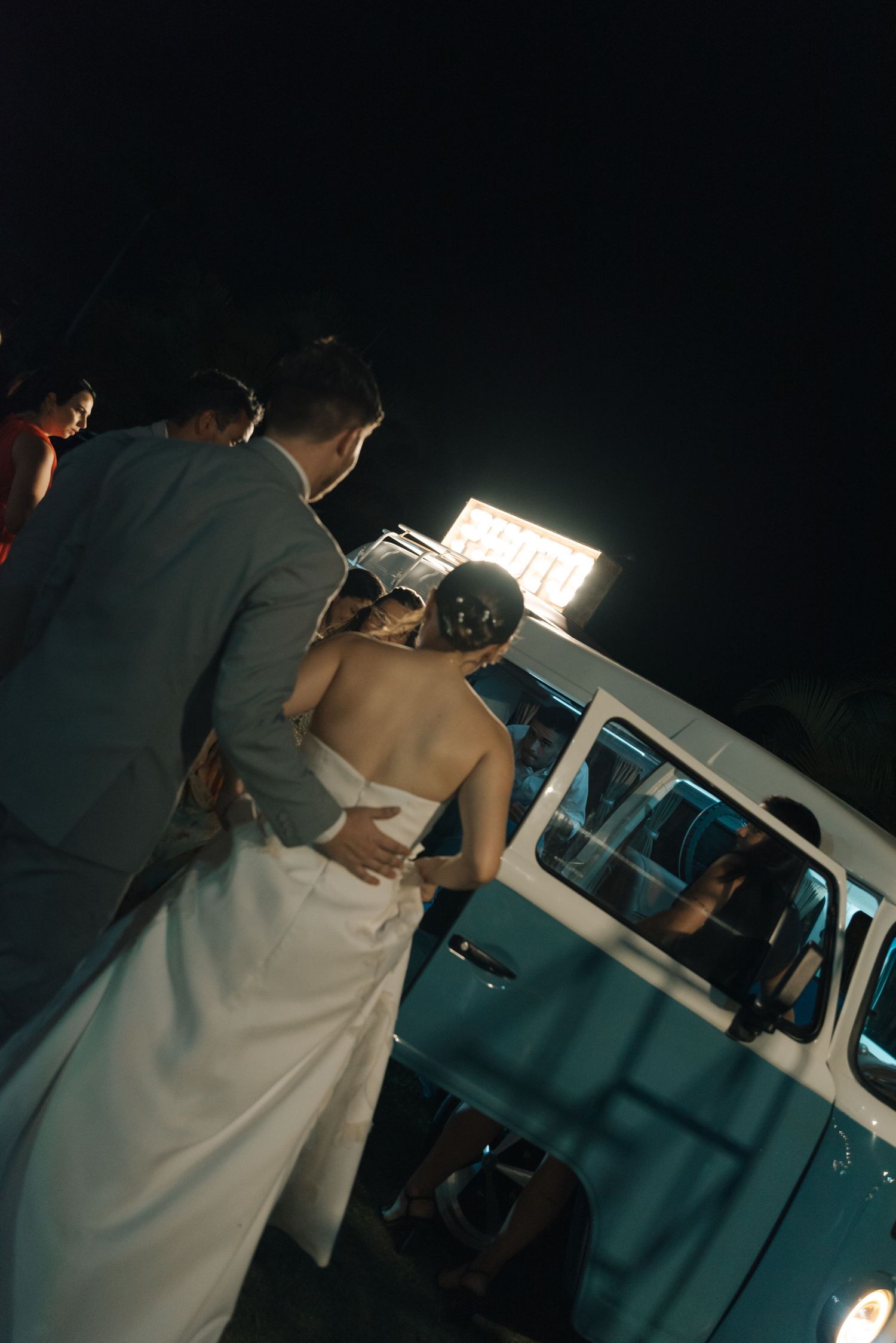 Night shot of wedding guests gathering around a vintage van with lighting.