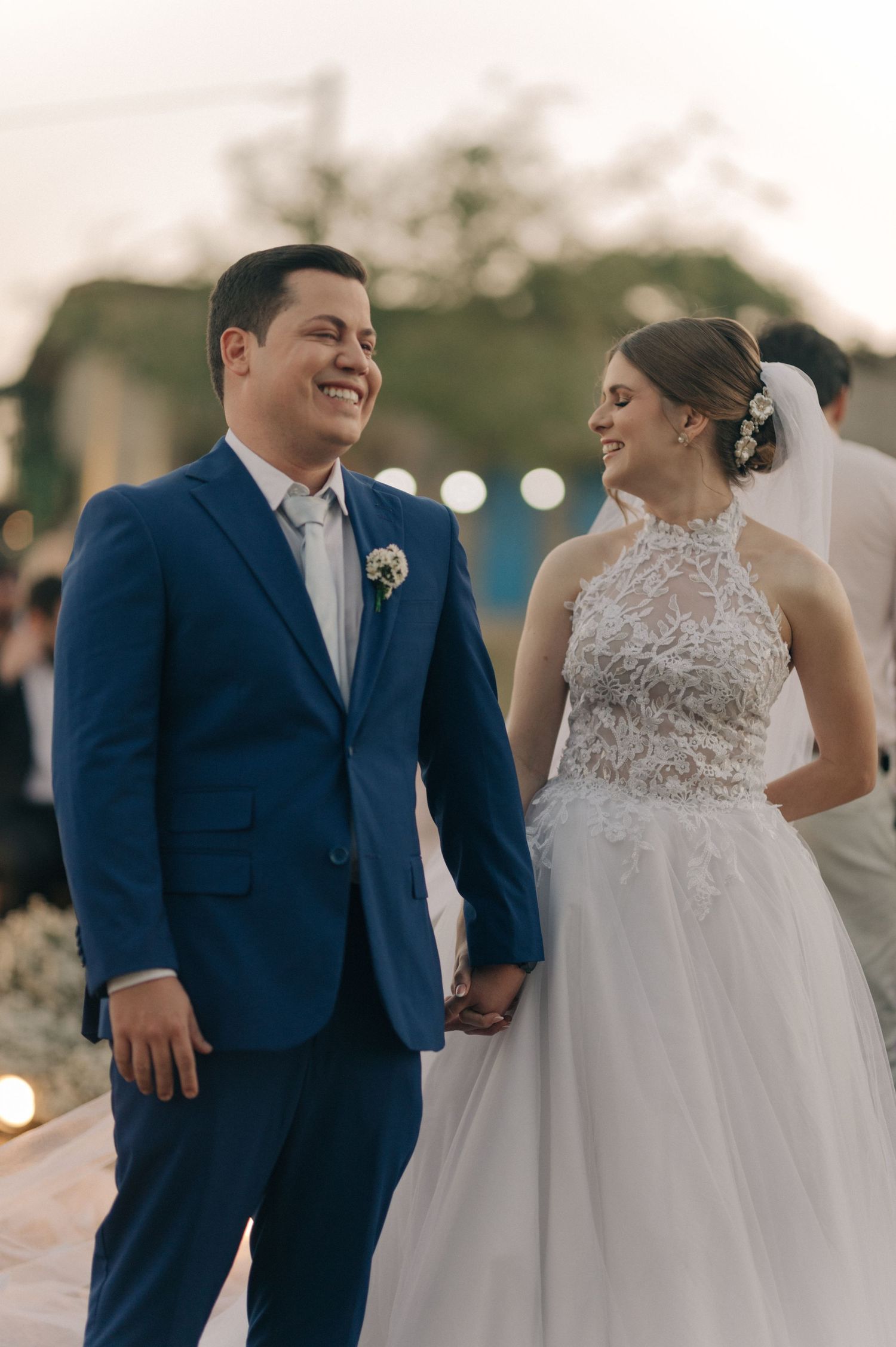 Newlyweds share a joyful moment during their wedding ceremony, with the bride in a lace gown and groom in navy suit.
