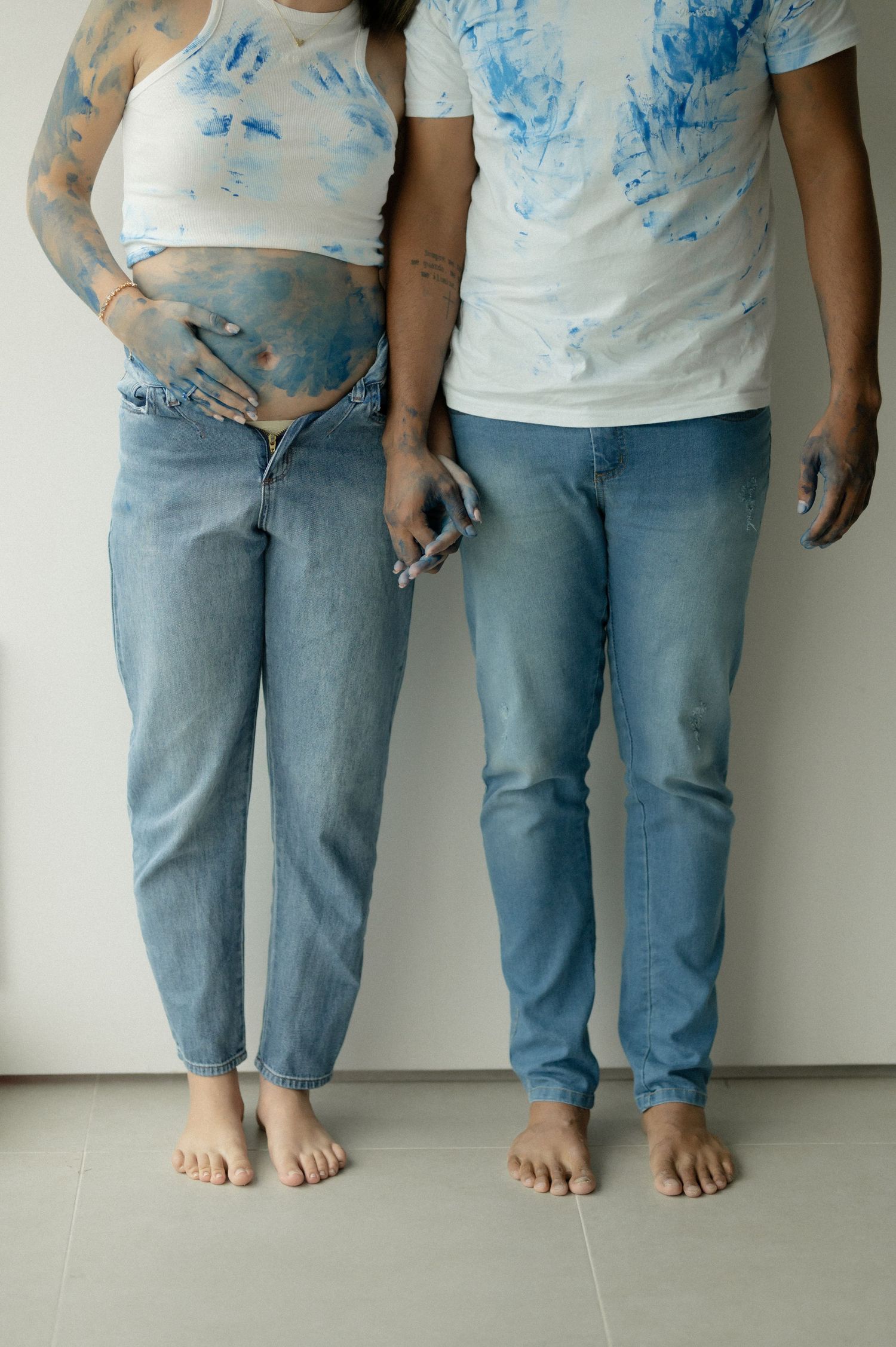 Three people wearing blue jeans and white t-shirts with blue paint stains stand against a white wall.