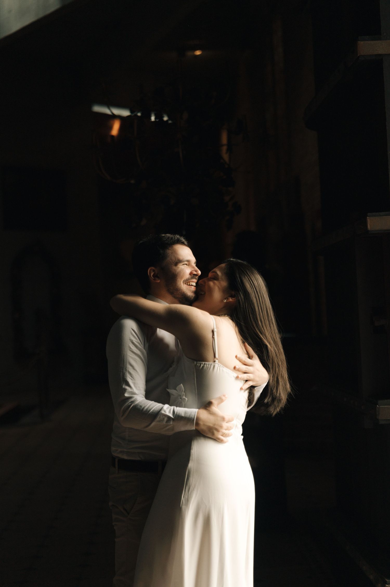 A couple embraces in a romantic dance pose with dramatic lighting casting shadows in a dark indoor setting.