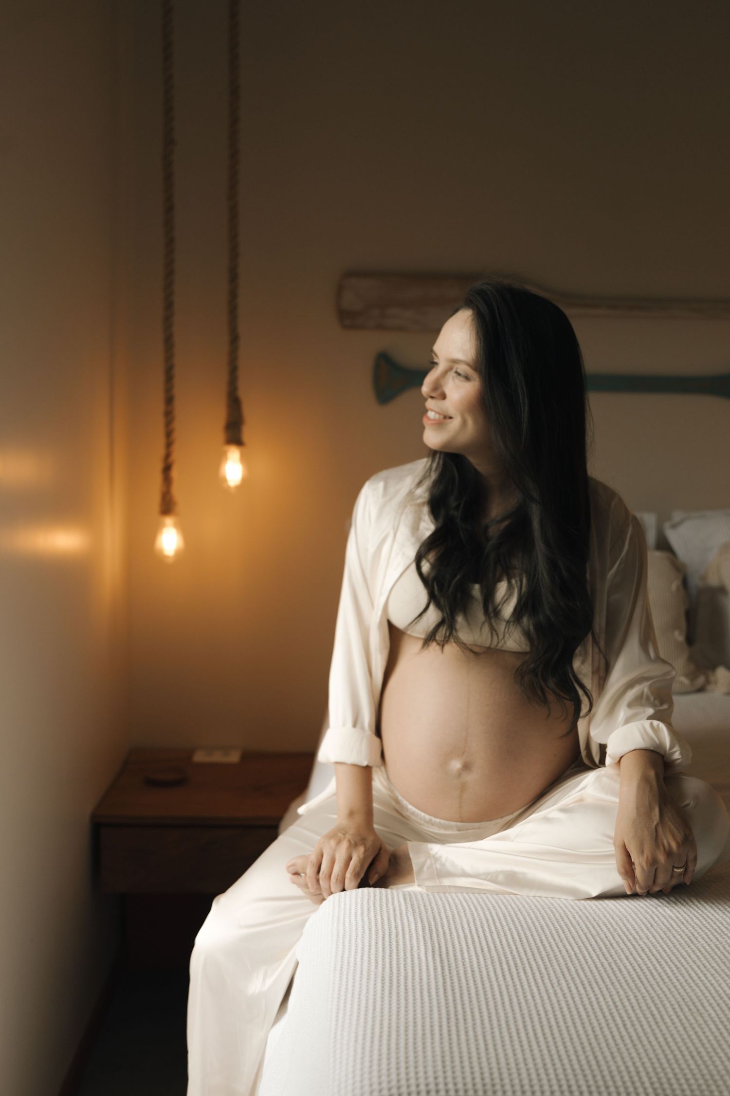 A moody boudoir scene with warm lighting features a person in white lounging on a bed.
