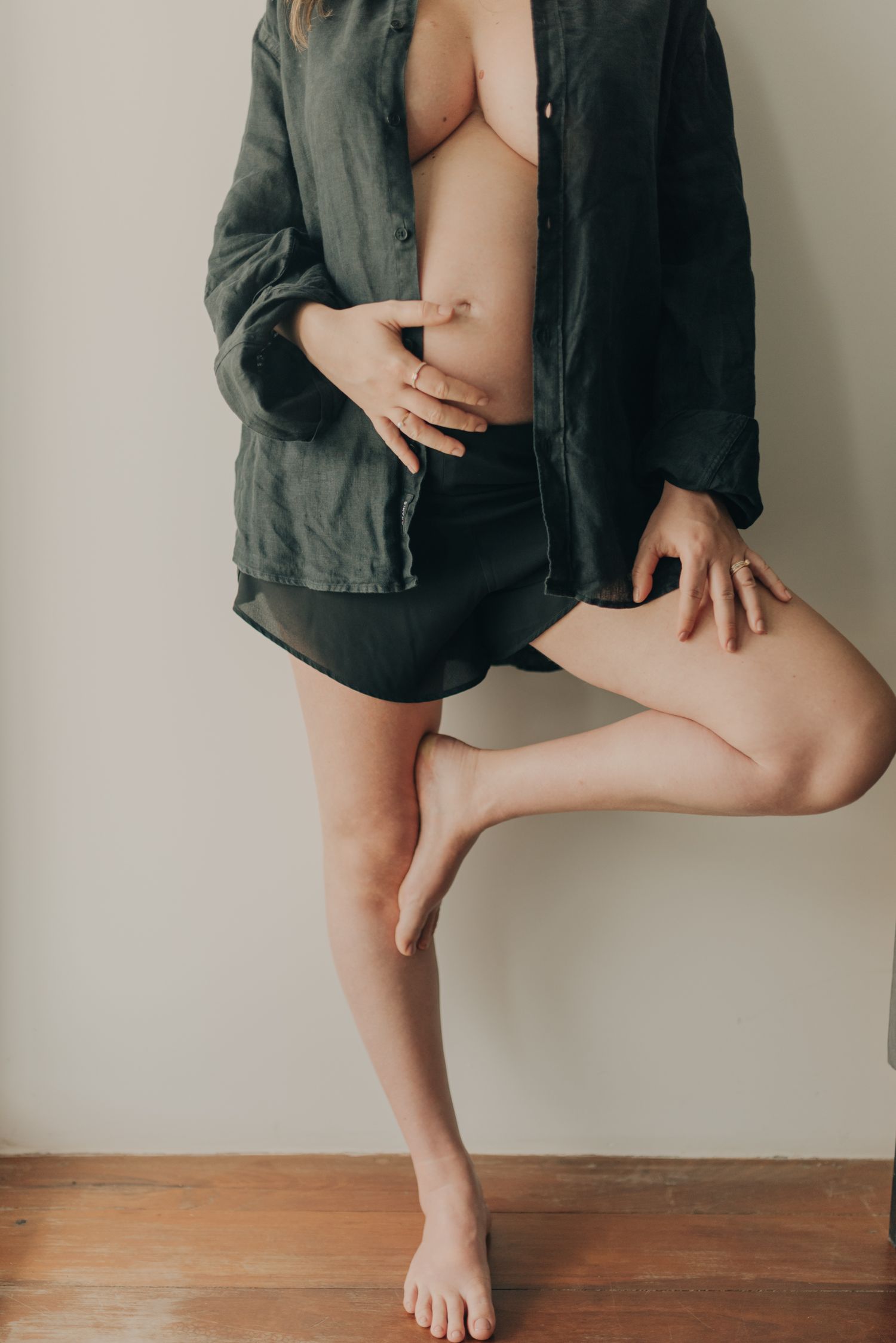 Artistic portrait of figure in black oversized shirt and shorts against minimalist backdrop.