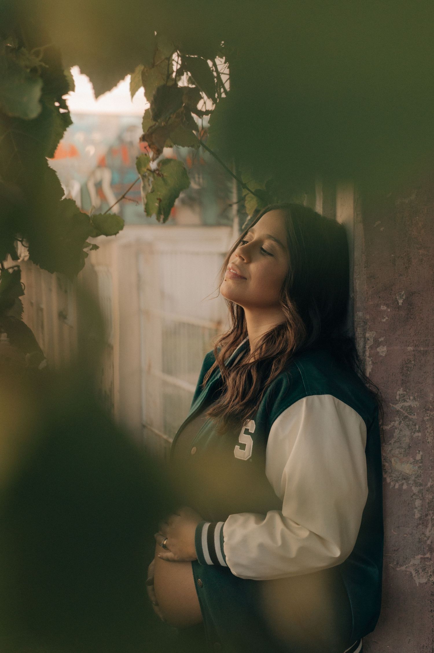 Artistic maternity portrait with moody lighting and foliage framing.