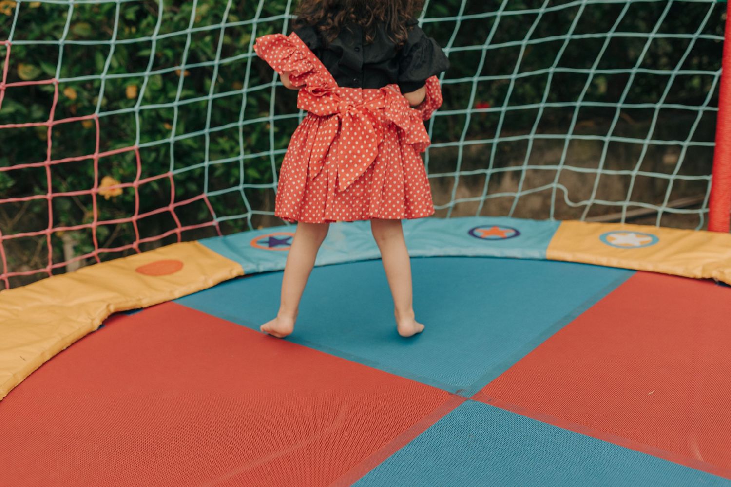 Child in coral dress playing on colorful trampoline surface outdoors.