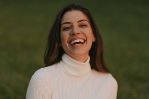 Close-up portrait in cream turtleneck sweater showing genuine laughter against green background.
