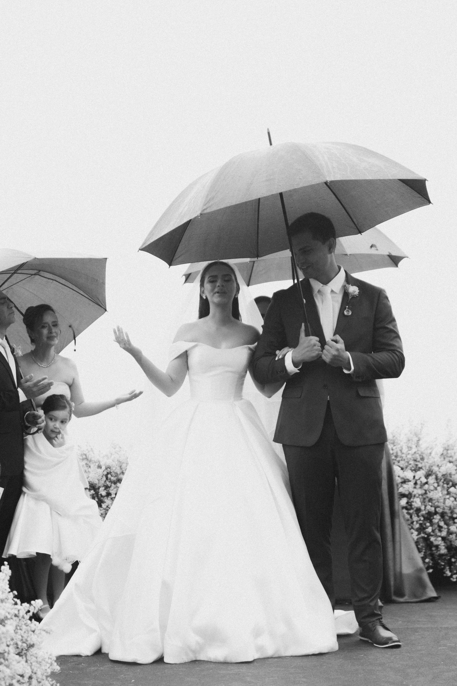 Wedding party poses with white umbrellas in a sequence of four candid black and white photographs outdoors.