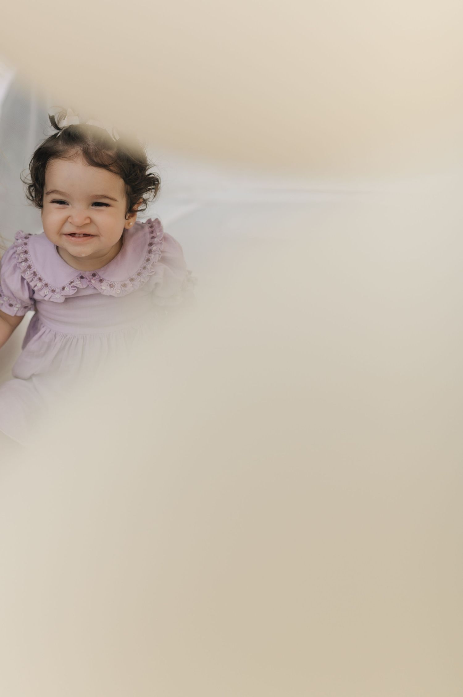 Young child in purple dress smiling against light background.