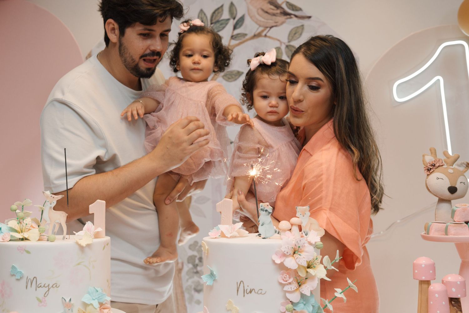 Family gathered around decorated birthday cakes at pink-themed party.