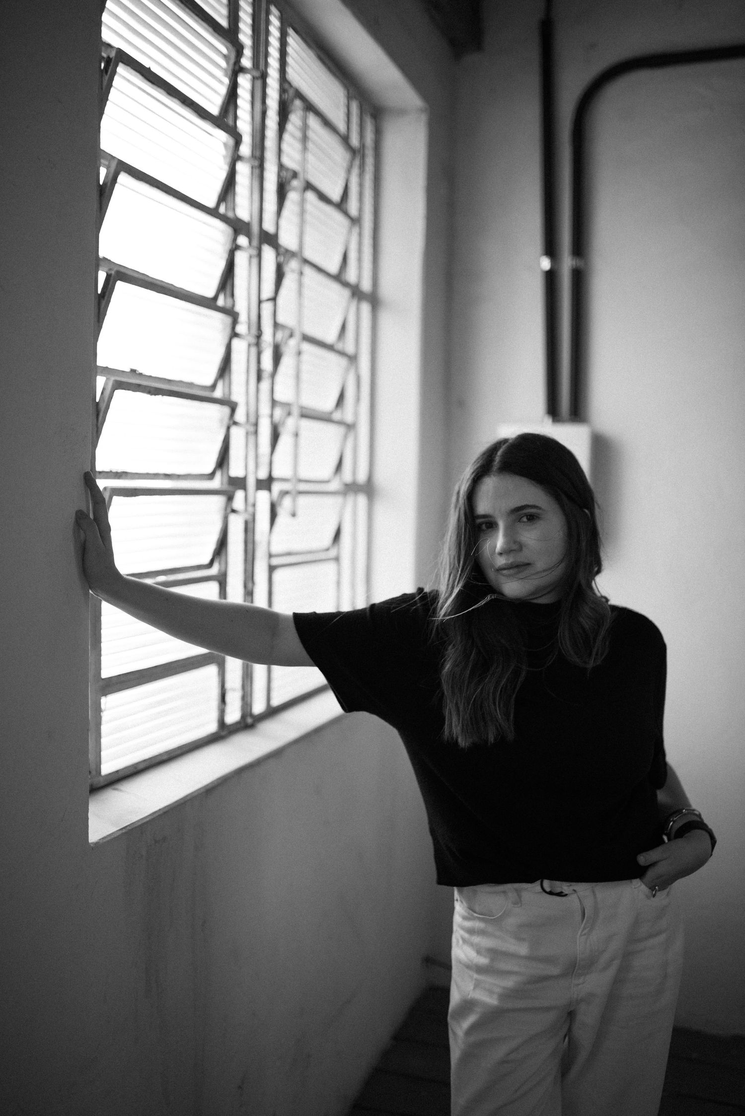 Artistic black and white photo of woman standing next to industrial window.