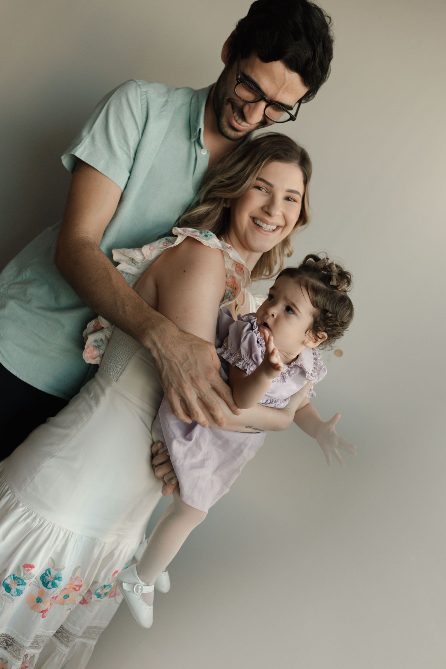 A loving family shares joyful laughter and embraces while posing against a neutral wall in casual attire.