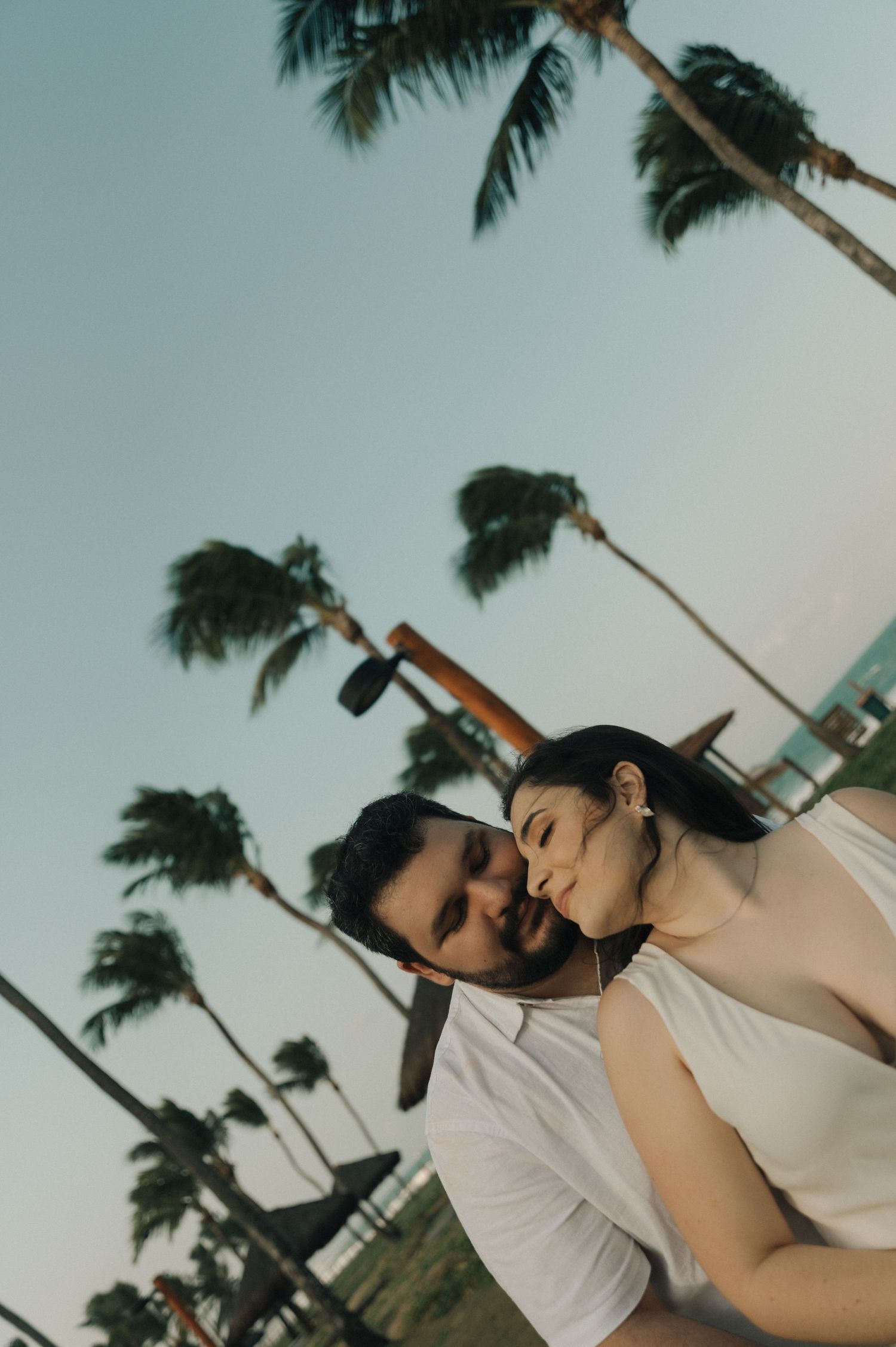 A romantic couple embracing under swaying palm trees on a tropical beach.