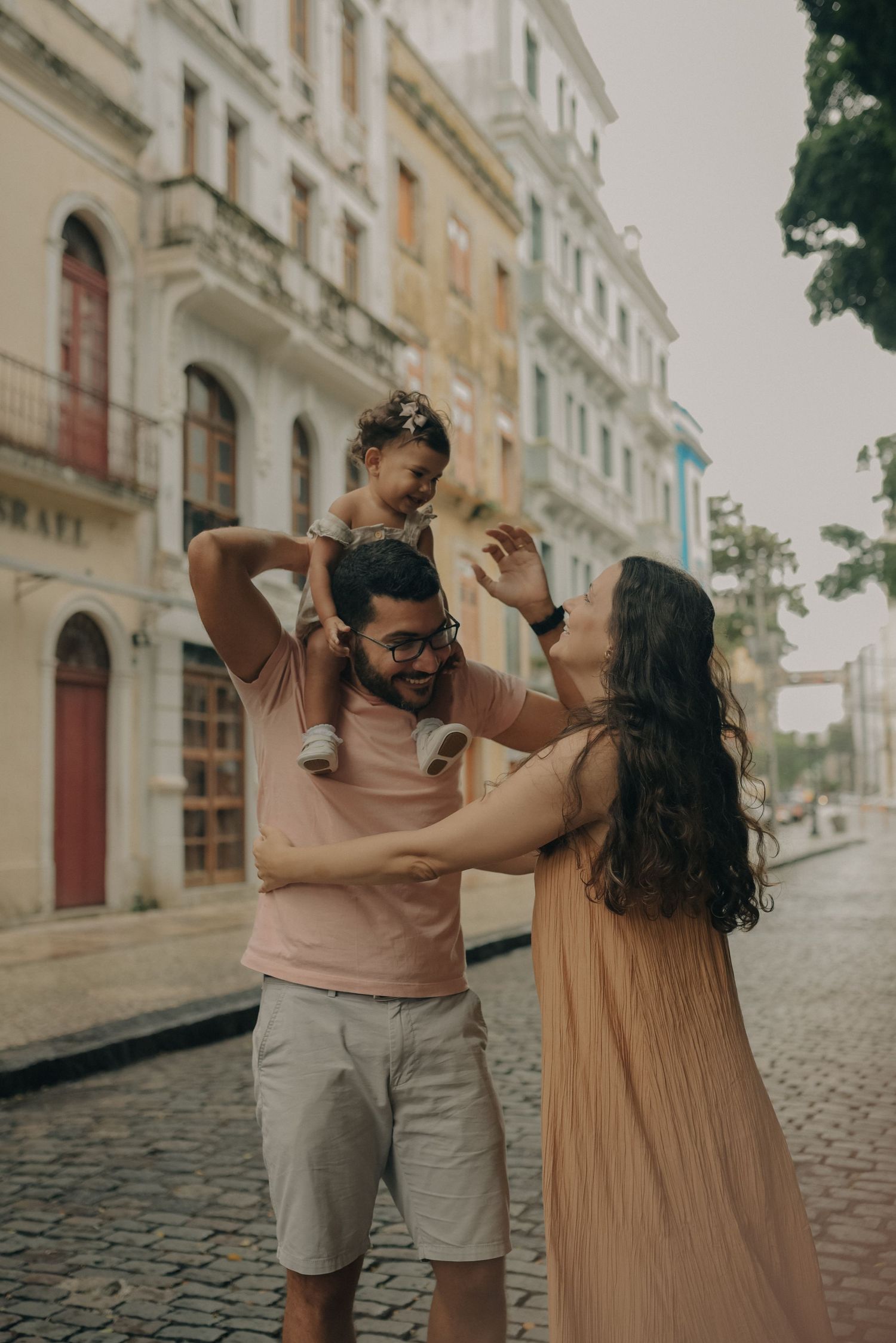Family sharing playful moments on a cobblestone street with historic buildings in the background.