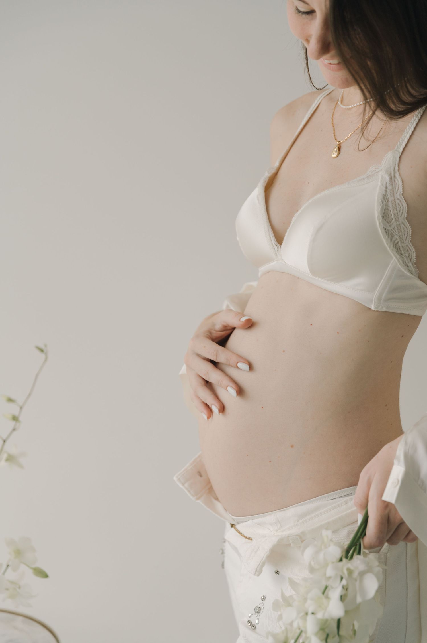 Delicate maternity boudoir photo with white flowers and lace details.