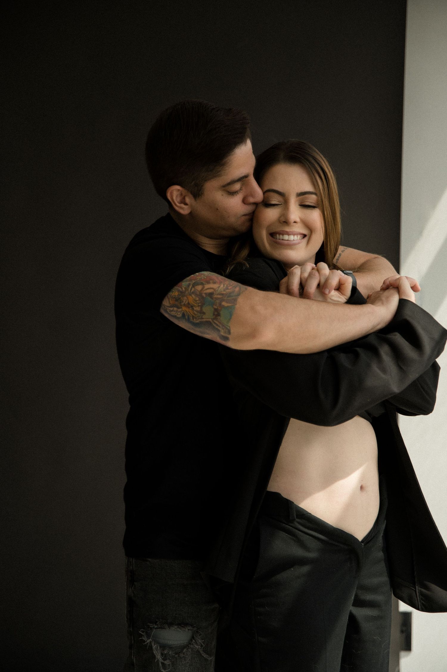 A romantic couple embraces and dances together in a dimly lit room with dramatic lighting and shadows.