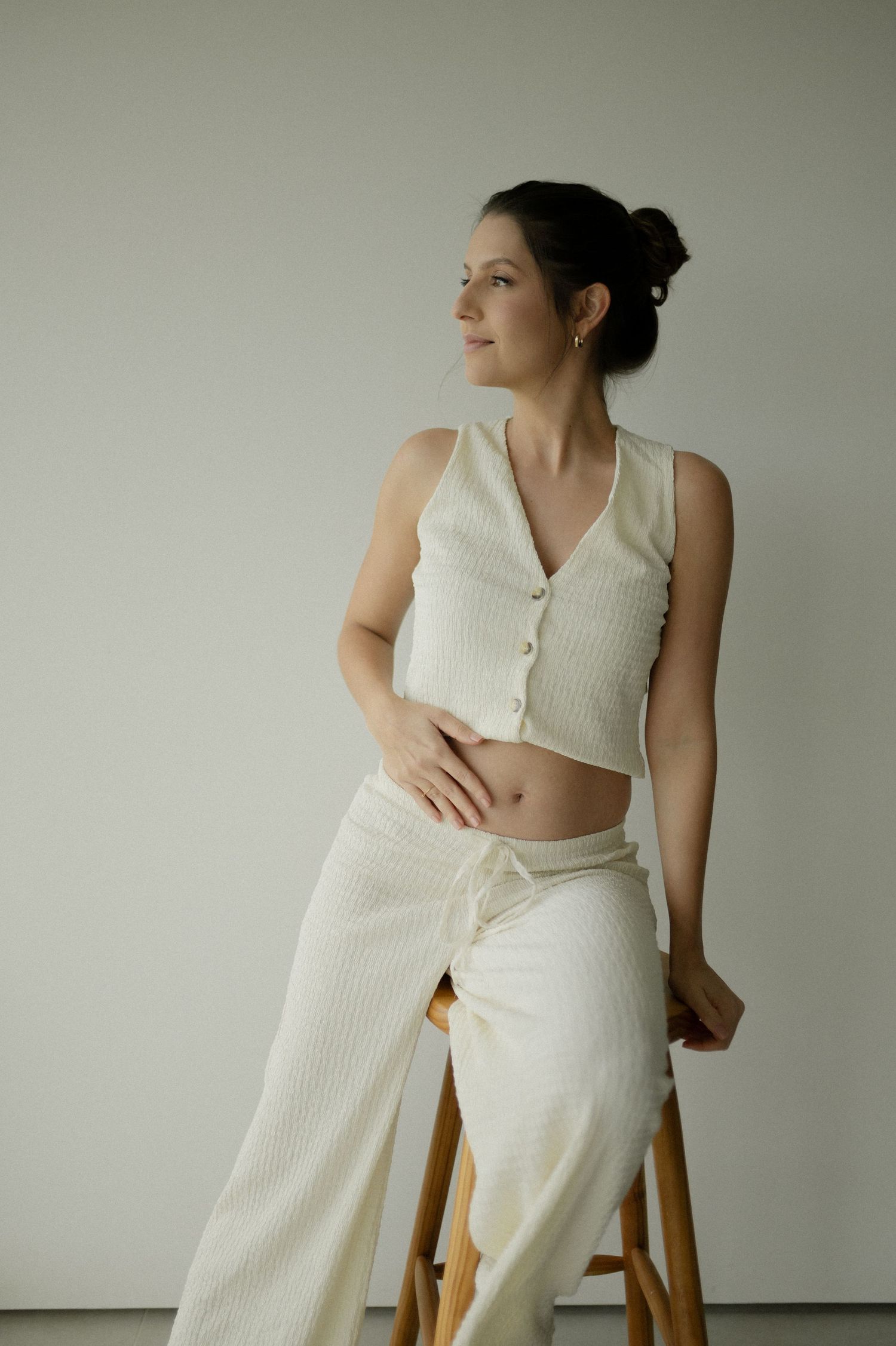 Minimalist fashion portrait showing a cream ribbed crop top and matching pants while sitting on a wooden stool.