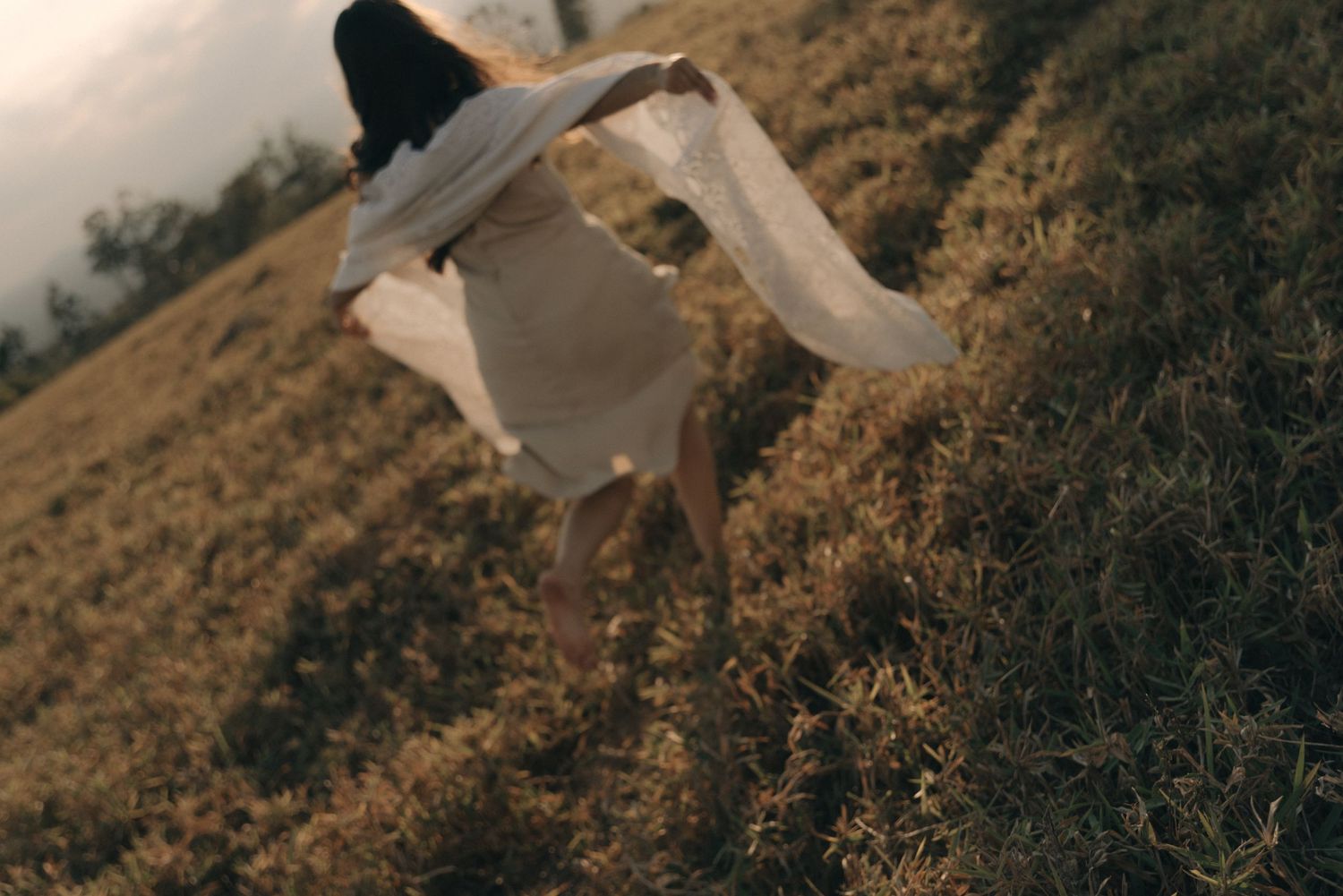 Artistic motion shot of person in flowing white fabric on hillside at sunset.