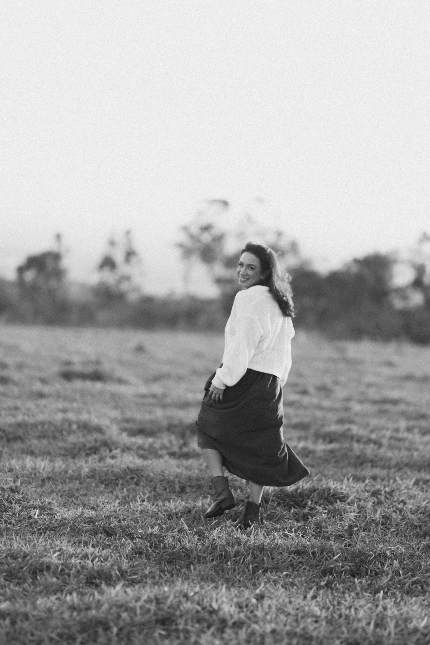 Black and white portrait of a person twirling in a field wearing a long skirt.