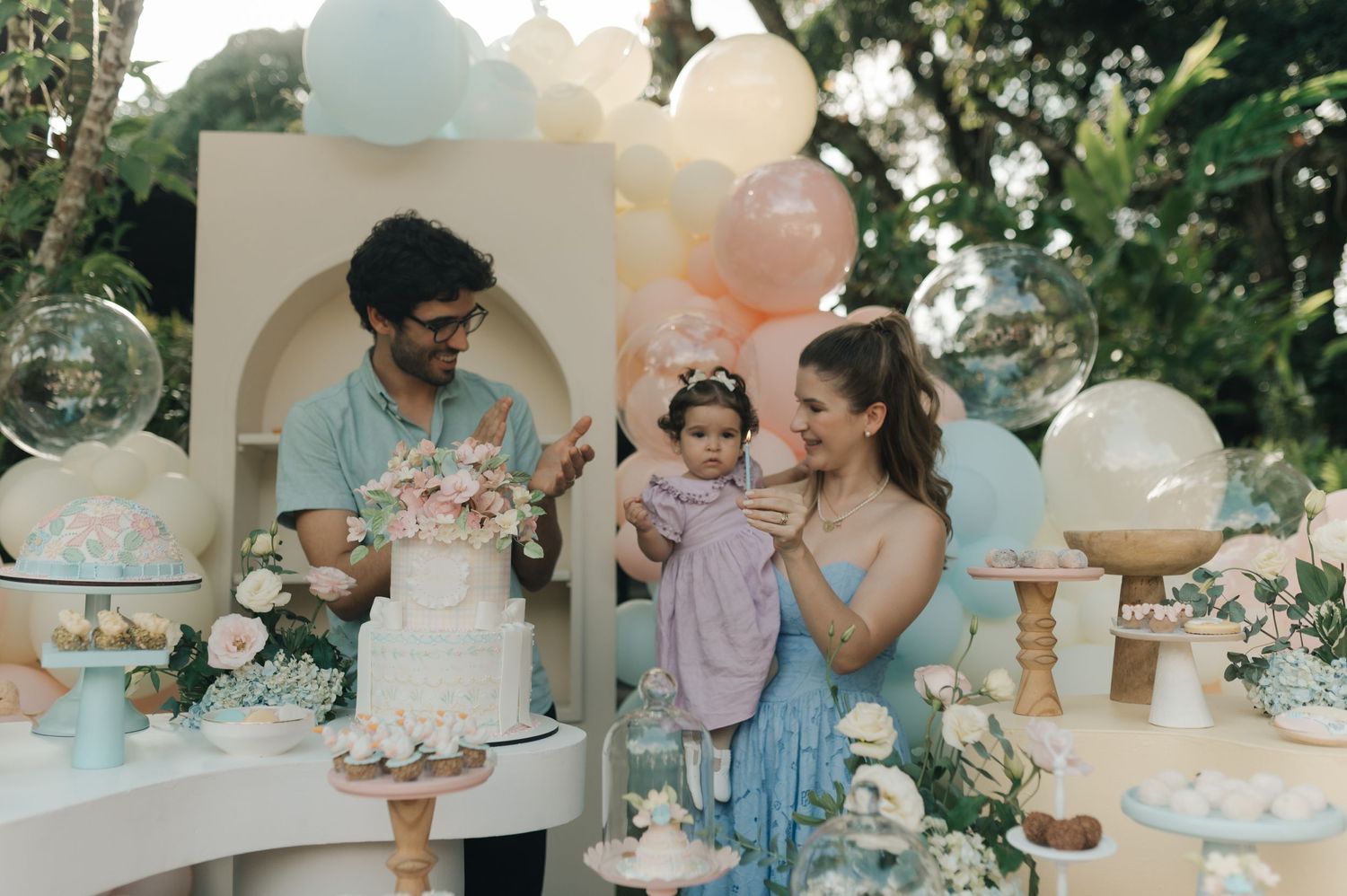 Family gathered around dessert table at outdoor celebration with balloon decorations.