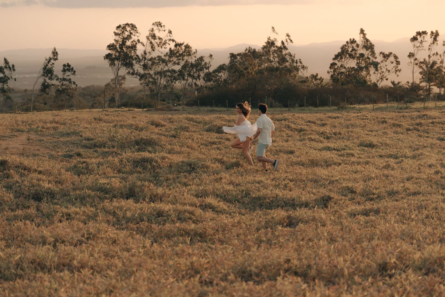 Couple in light colored clothing running through a golden field at sunset.
