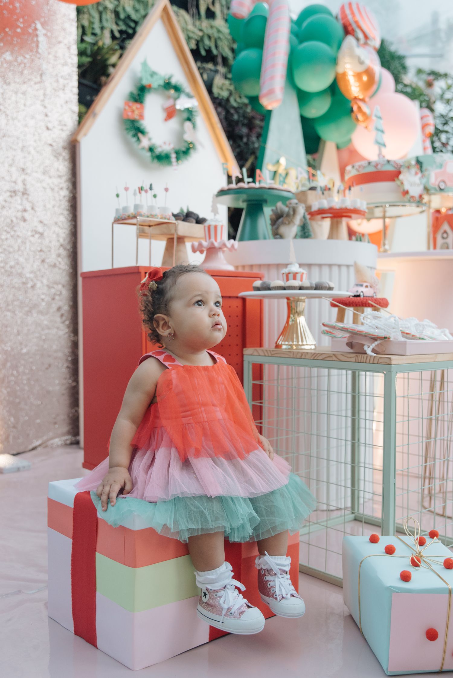 A whimsical birthday setup with a small child in a colorful tulle dress sitting on decorative present boxes.