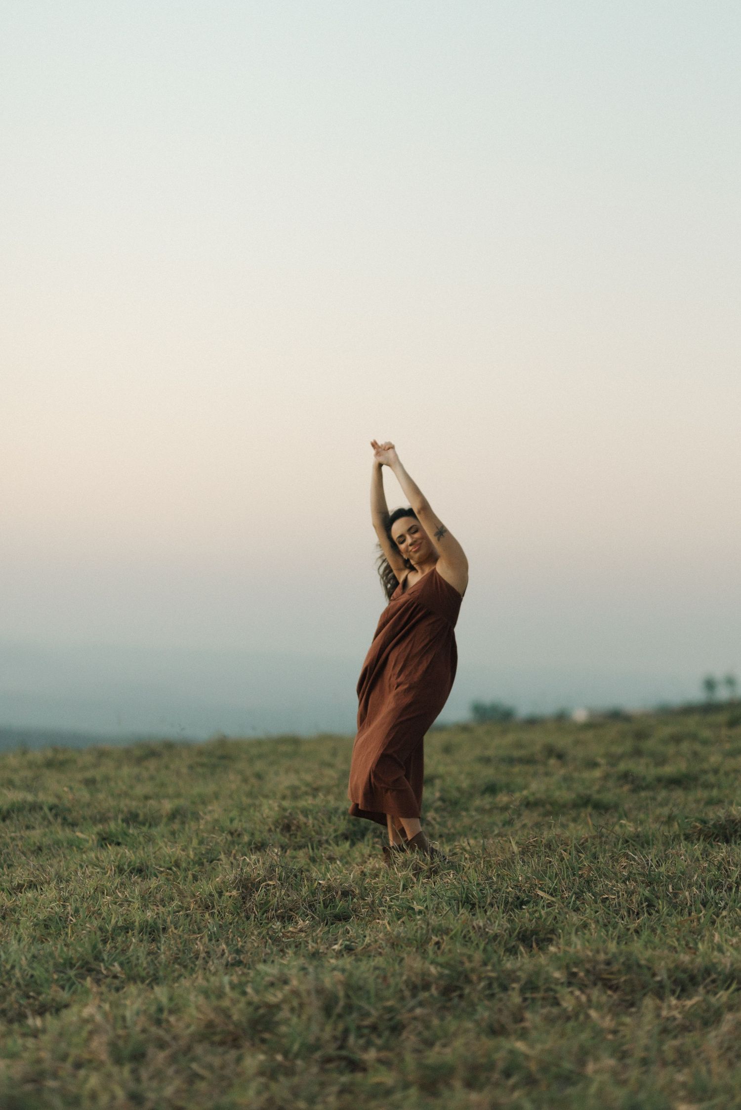 Silhouette of a person in a flowing dress stretching against a sunset sky.