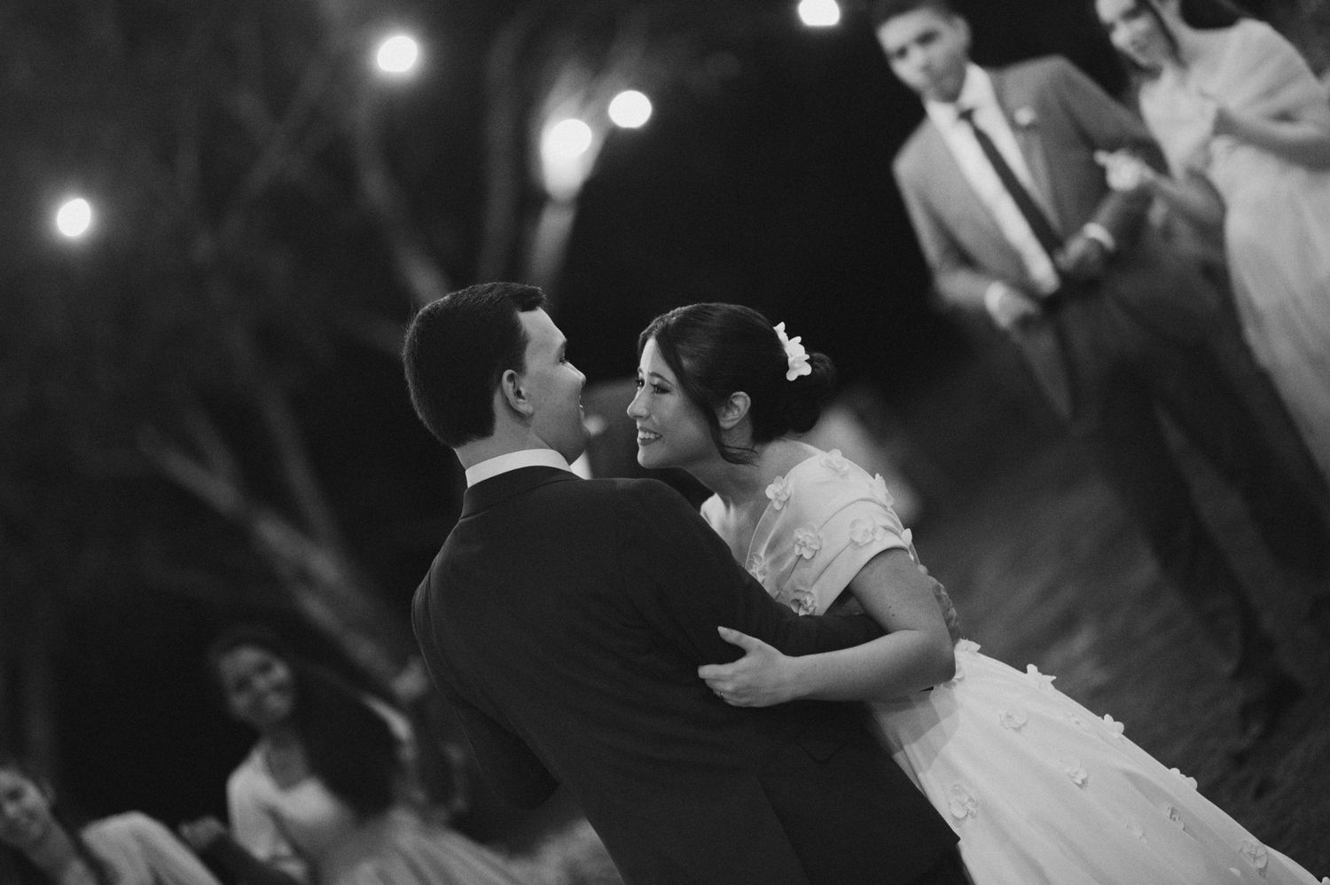 A romantic black and white dance scene at a wedding reception with twinkling lights in the background.
