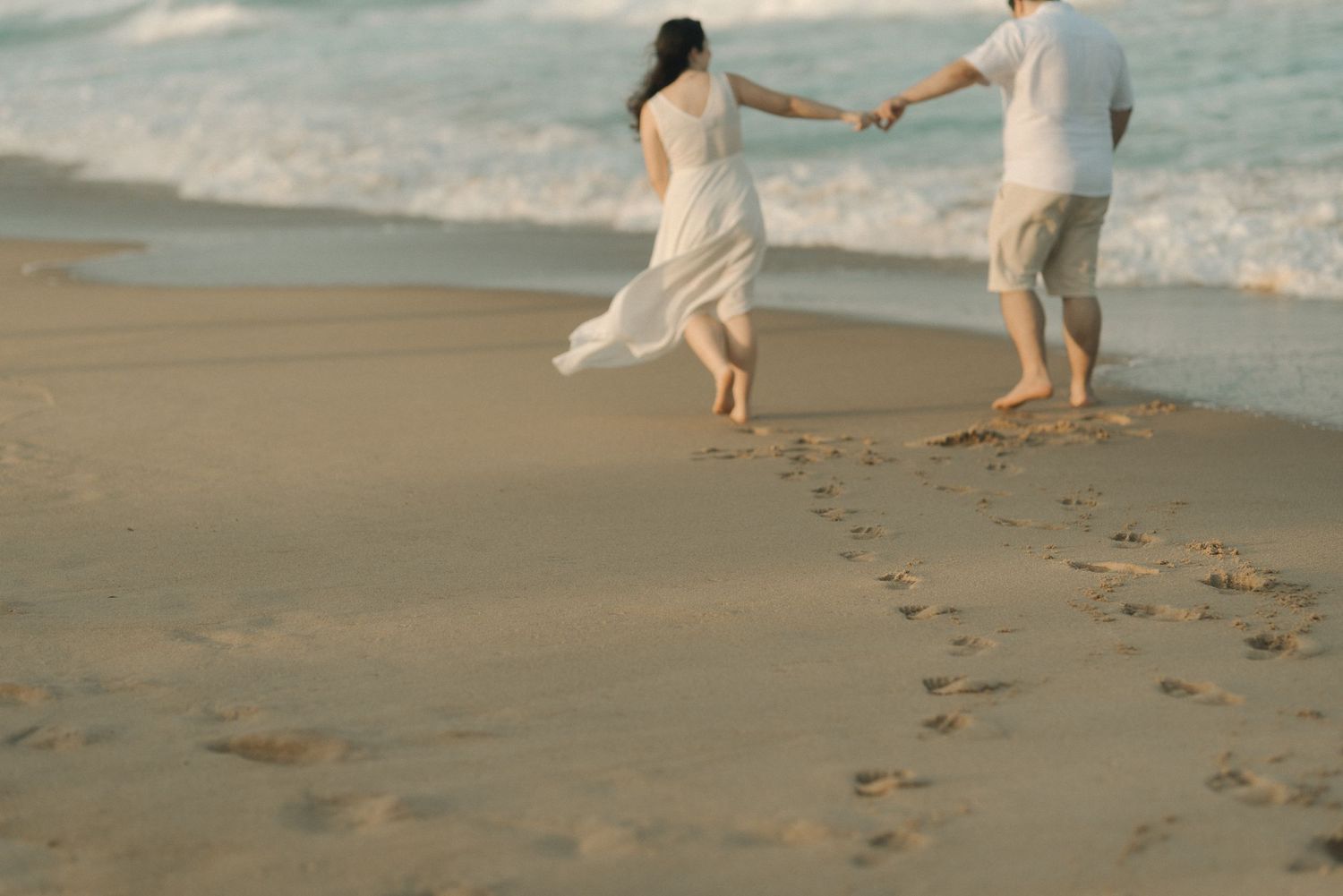 Couple walking on beach leaving footprints in sand during sunset.