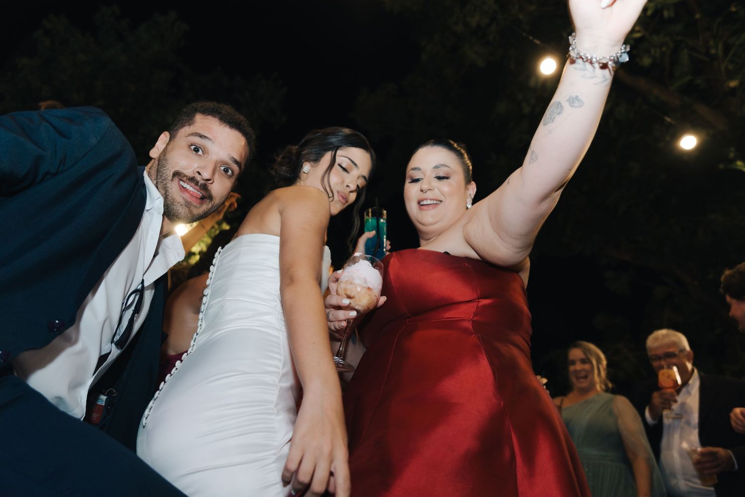 Wedding guests dancing and celebrating with drinks at an outdoor reception.