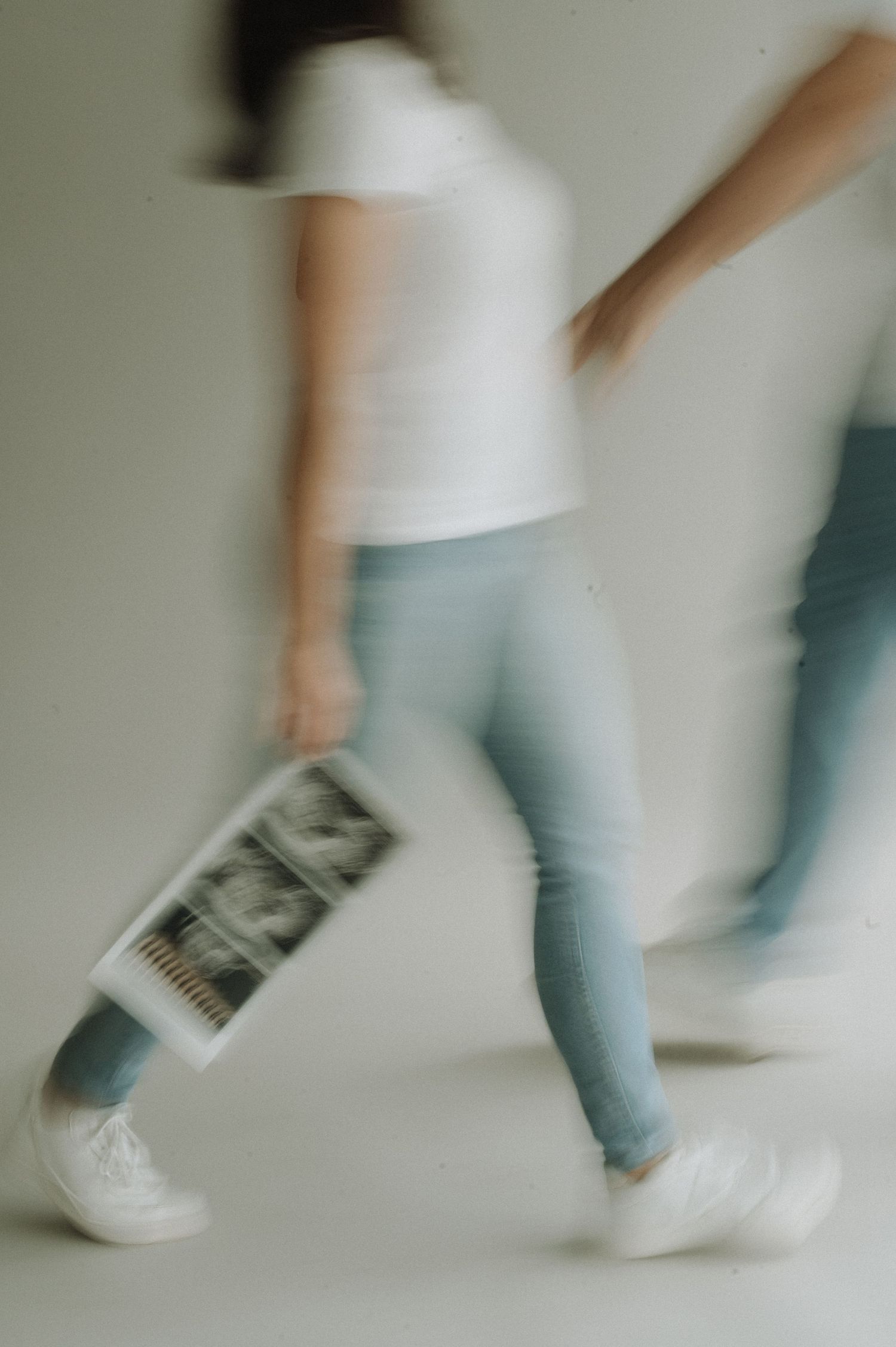 Motion blur captures feet in white sneakers and light blue jeans walking across a bright interior space.