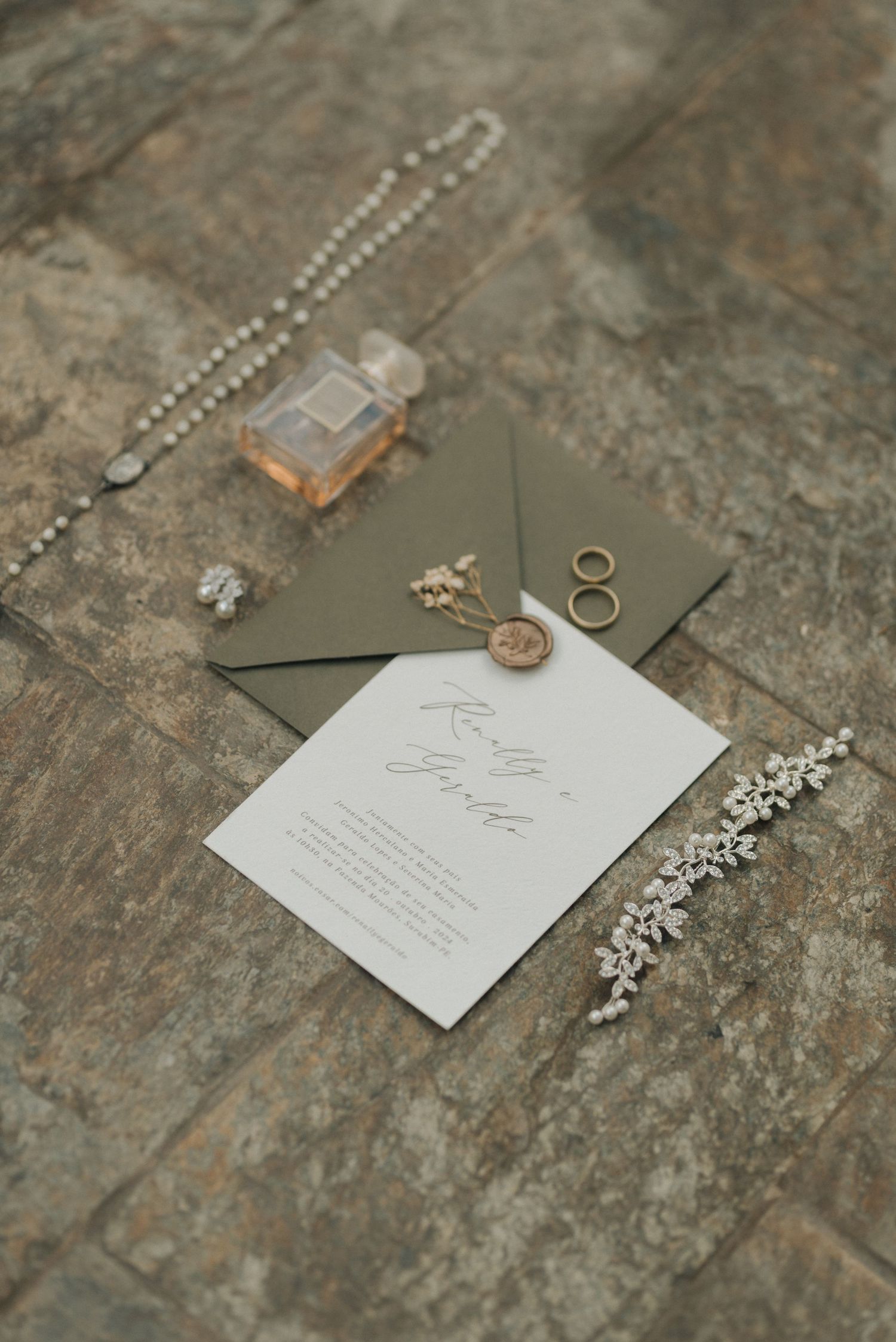 Wedding invitation with rings, jewelry and elegant accessories arranged on textured stone surface.