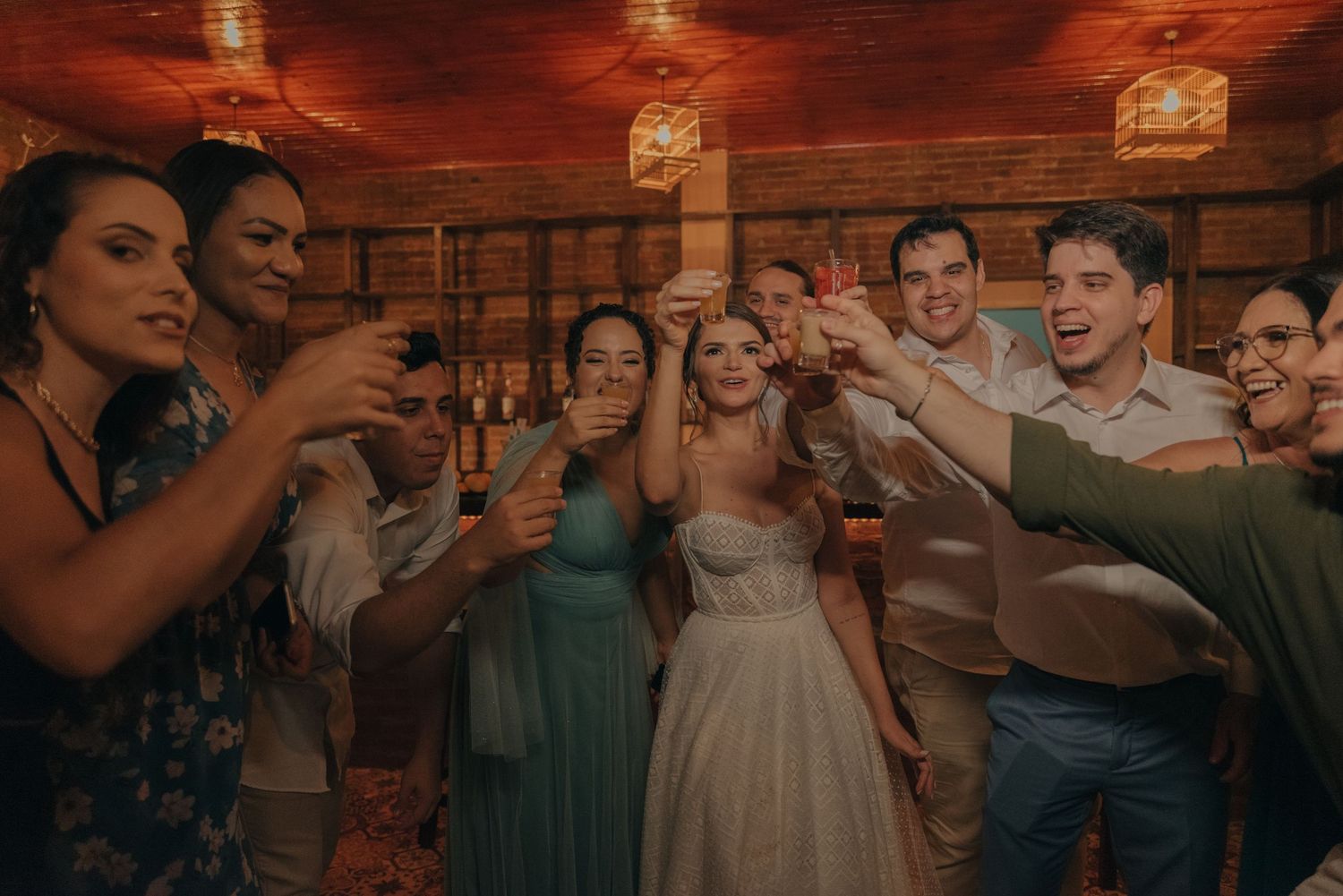 Wedding celebration with group toasting in rustic venue with warm lighting.