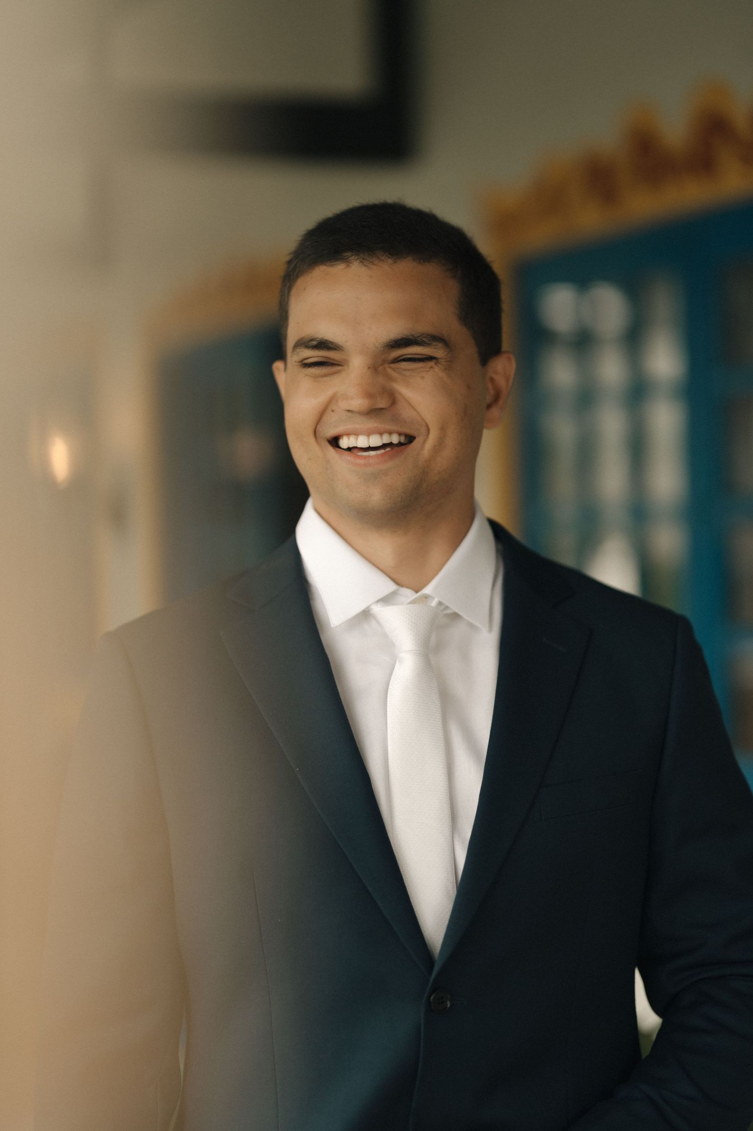 Professional wearing a dark suit and white dress shirt smiles warmly in an office setting.
