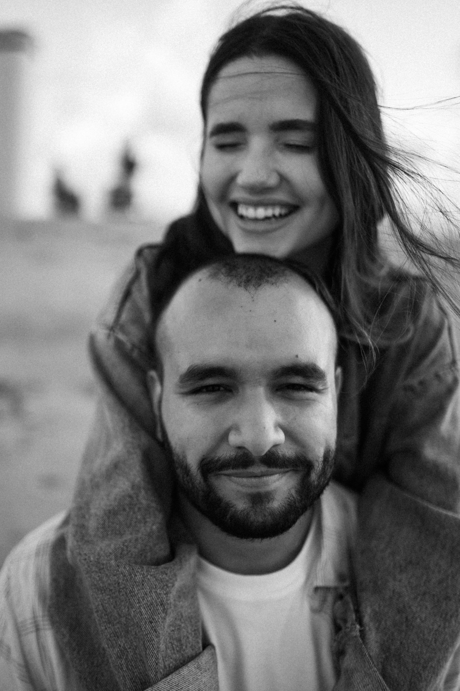 A black and white photo series showing a couple laughing and embracing outdoors with windswept hair.