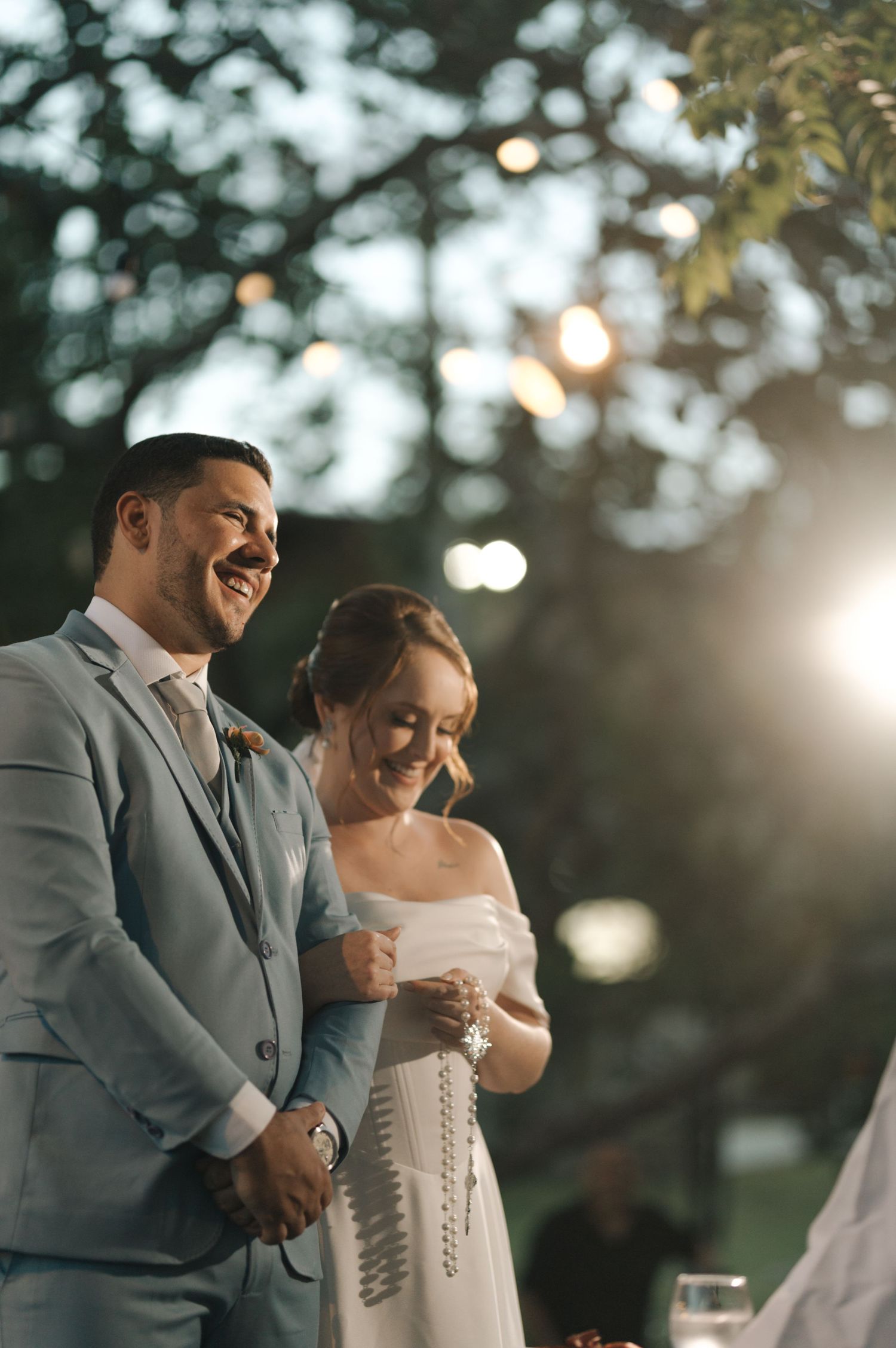 Candid wedding moment captured during sunset with soft bokeh lights in background.