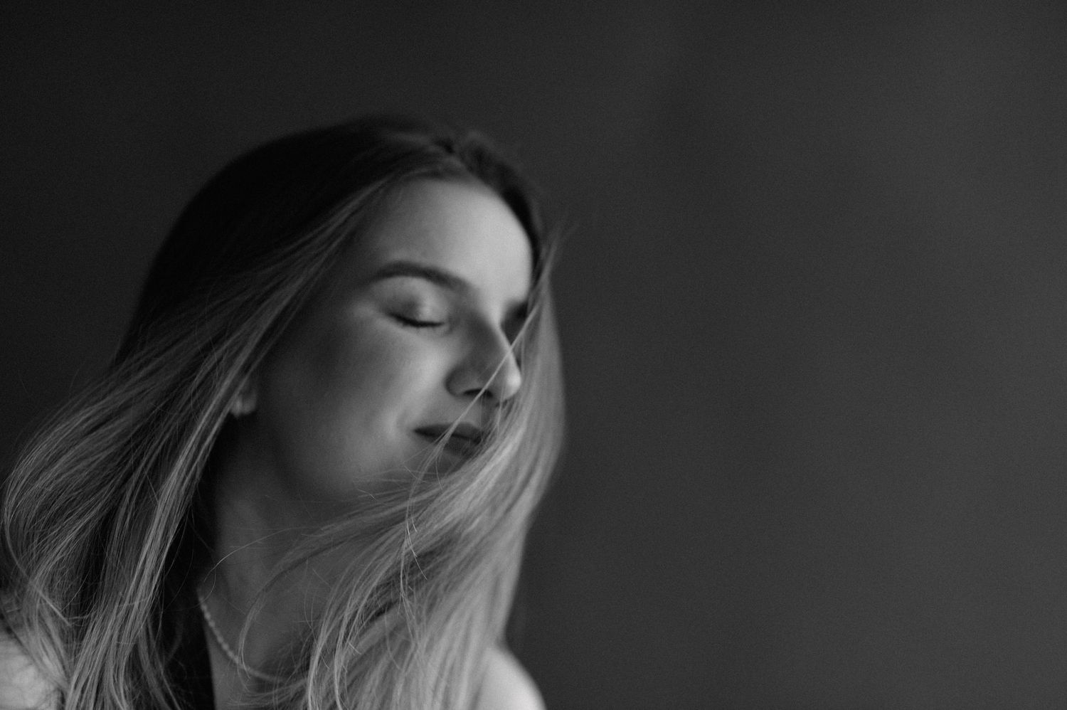 Artistic black and white profile portrait of woman with long blonde hair against dark background.