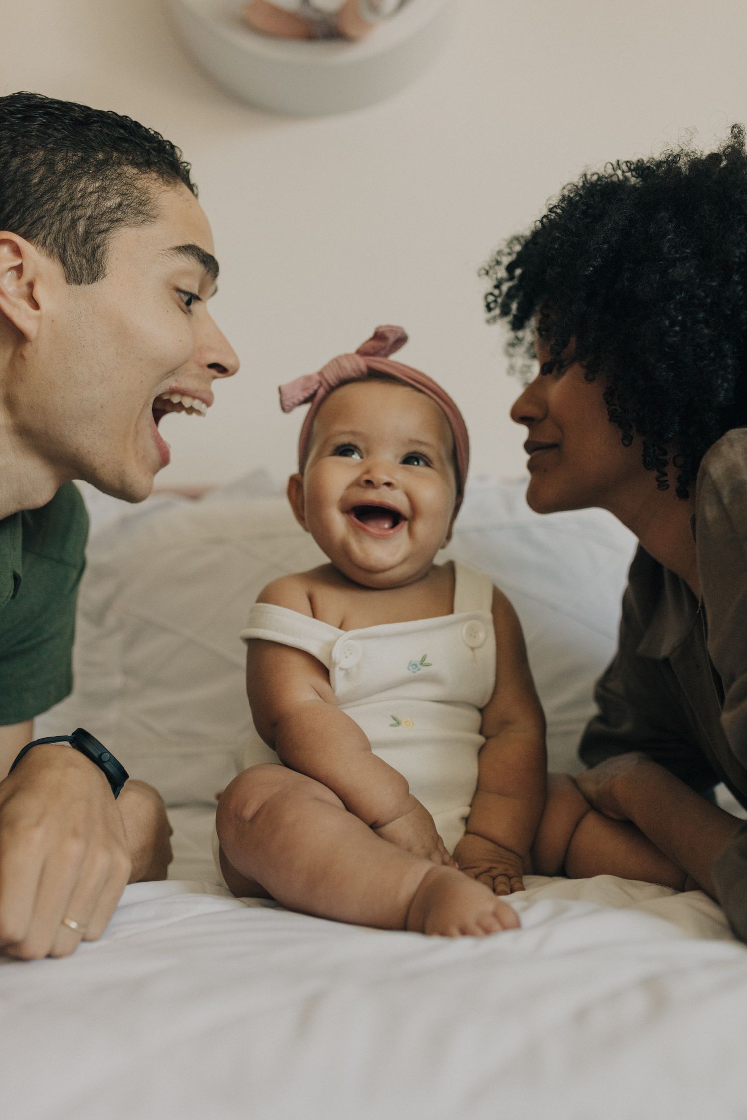 Happy family playing with their smiling baby on a white bed.