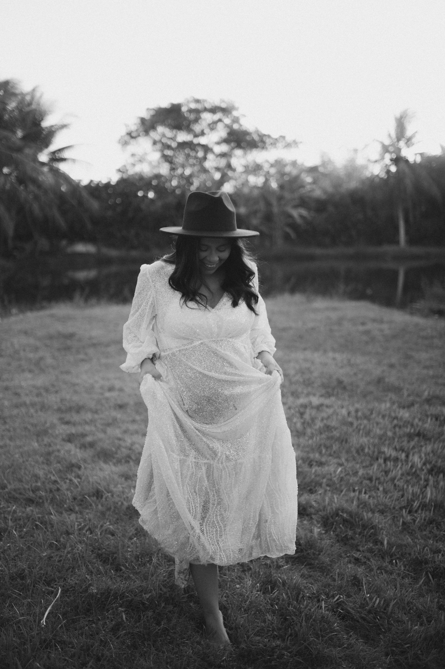Black and white portrait of figure in flowing white dress walking barefoot on grass.