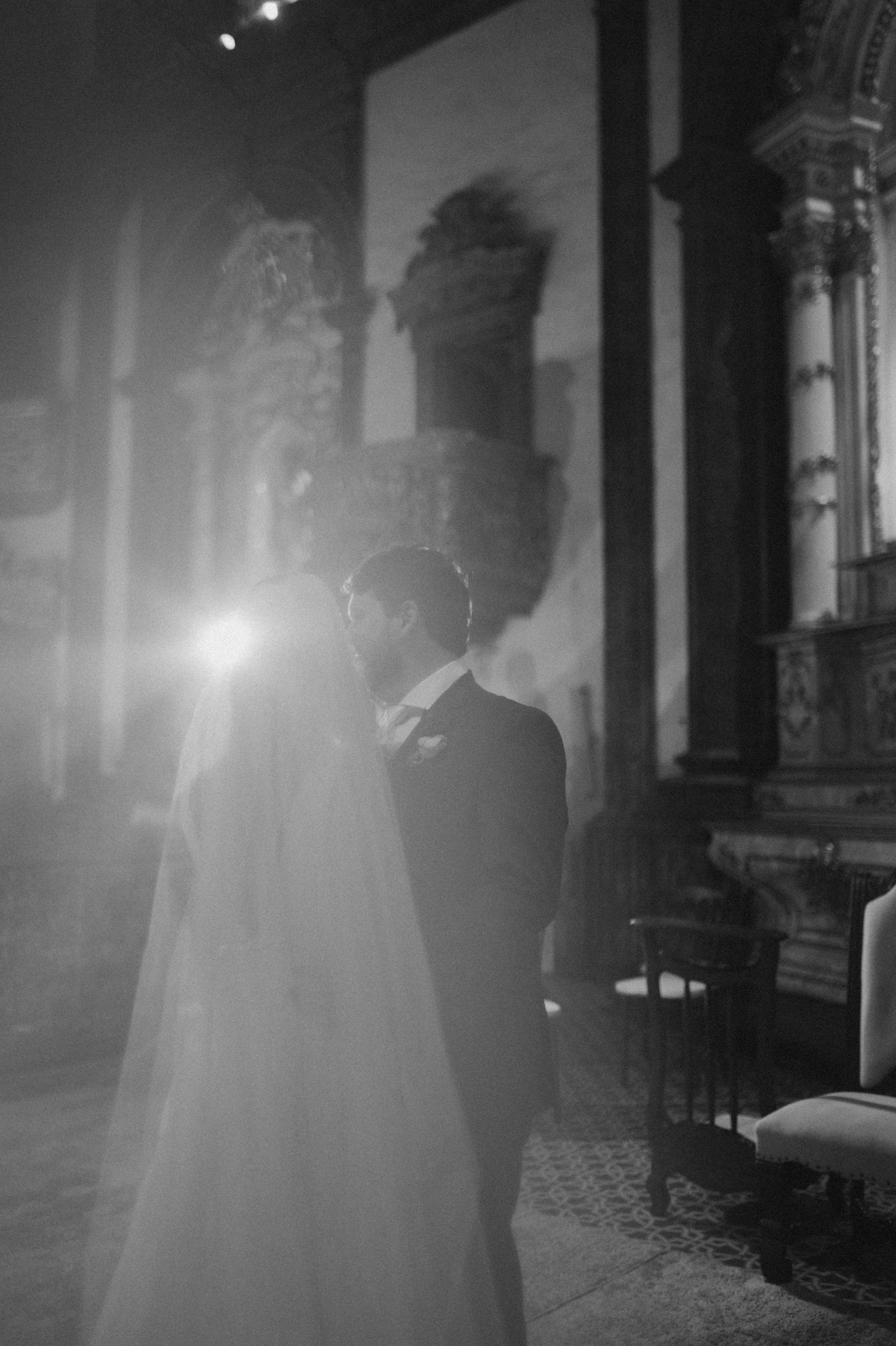 A romantic black and white wedding photograph capturing a couple in an elegant church with dramatic lighting and architecture.
