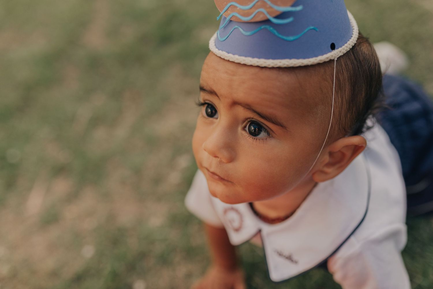 Child wearing blue party hat looking up with curious expression.