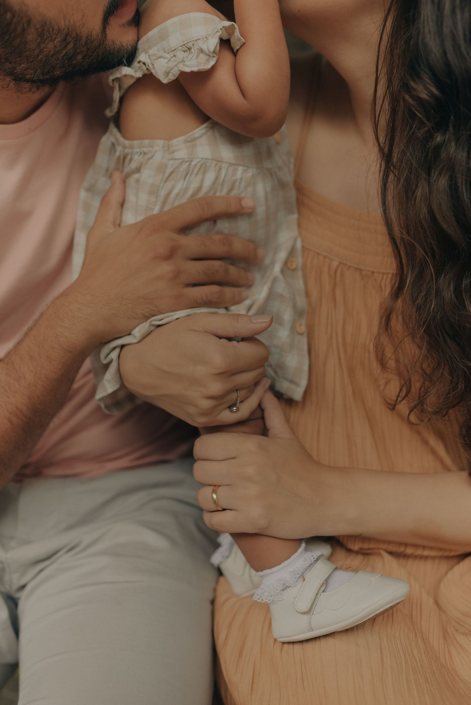 Close-up of hands holding a baby wearing white shoes and ruffled dress.