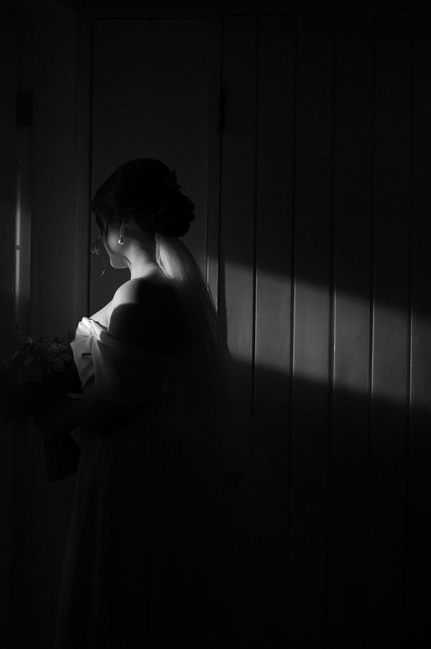 Artistic black and white silhouette of a bride in dramatic window lighting.