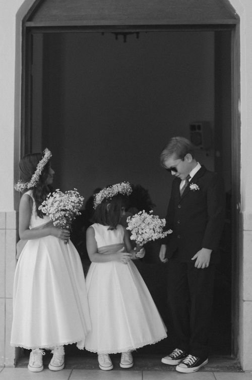 Black and white photo of flower girls with bouquets standing with a groomsman in sneakers.