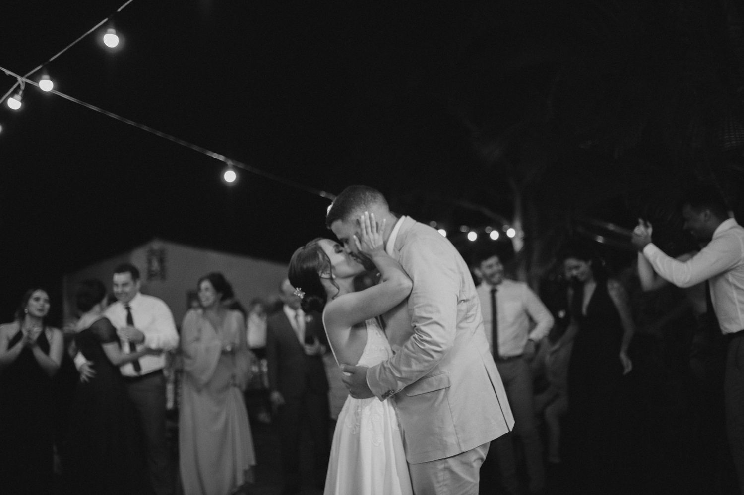 A black and white capture of a romantic dance moment at an outdoor reception with string lights.