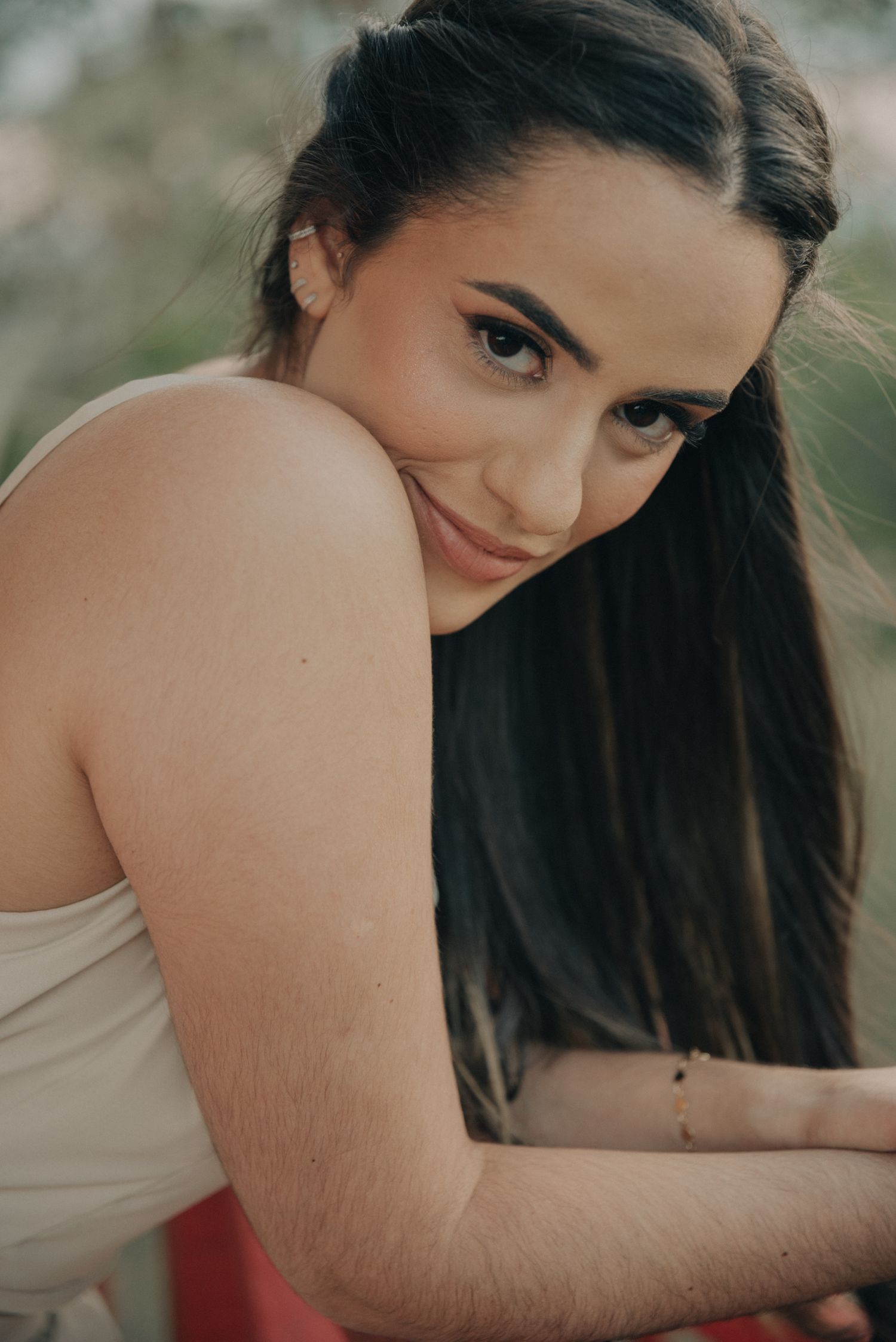 Close-up portrait showing bare shoulder and long dark hair against natural background.