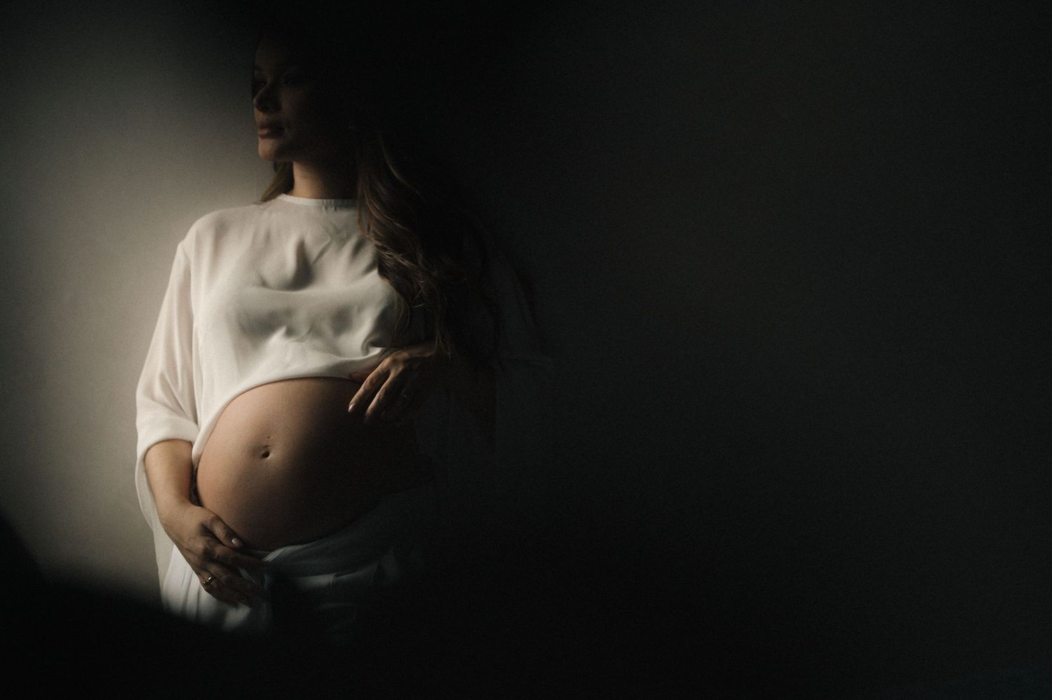 A series of artistic black and white maternity photos showing a pregnant belly in different poses and lighting.