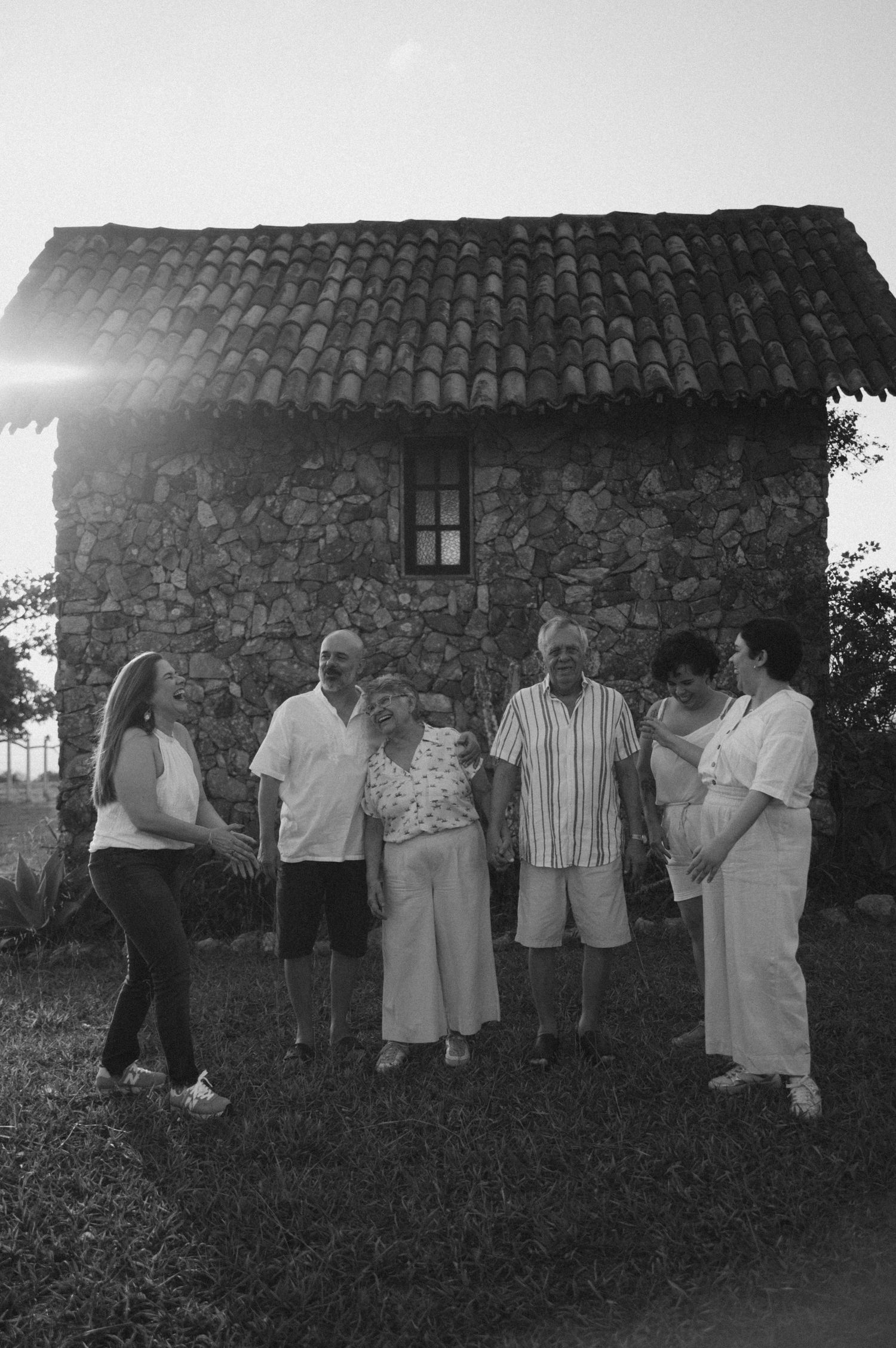 A group of people standing in front of a rustic stone building with a tiled roof in black and white photography.