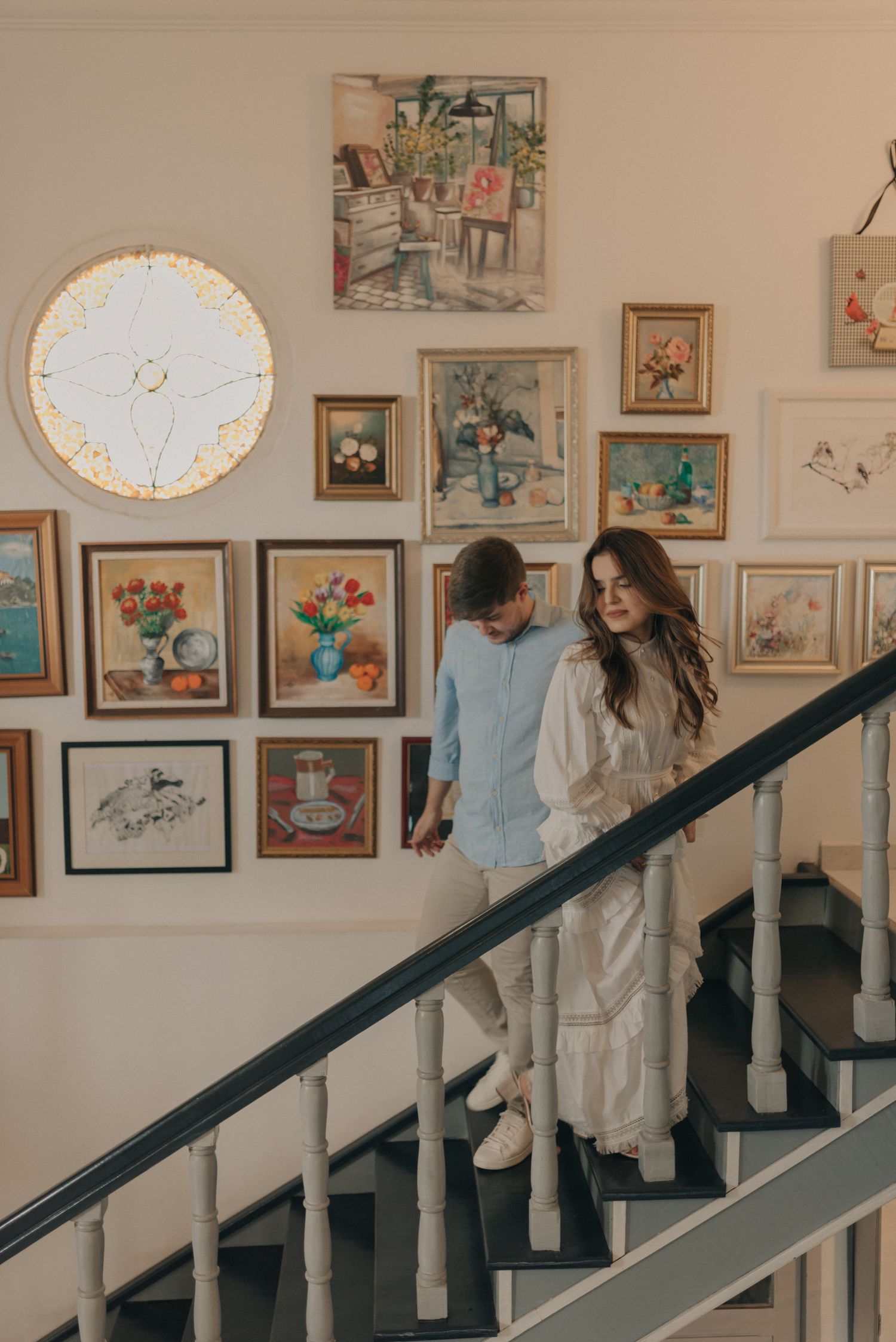 Couple on staircase surrounded by vintage art gallery wall with illuminated circular clock.