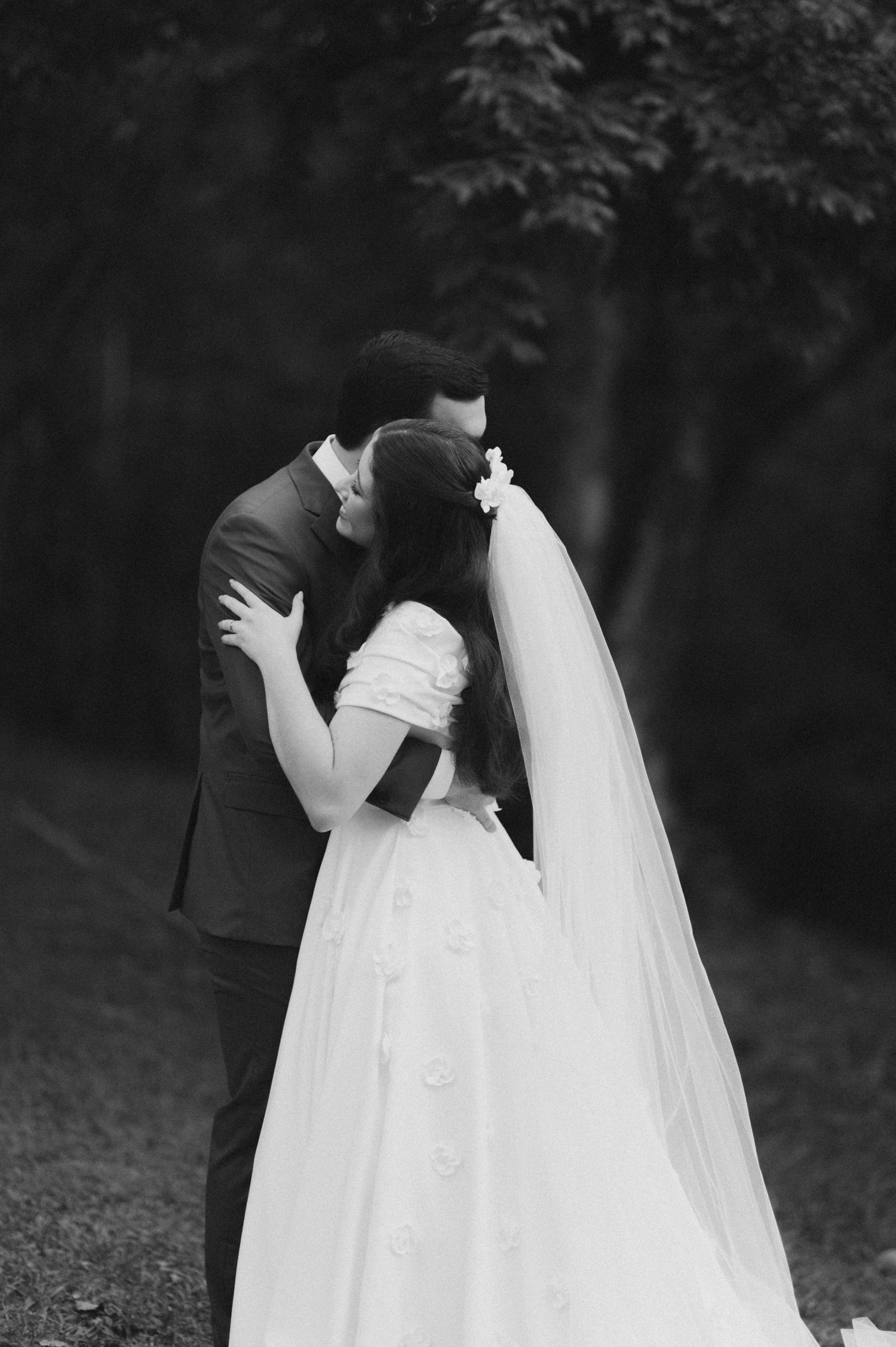 A romantic black and white wedding photo capturing a kiss between newlyweds in a garden setting.