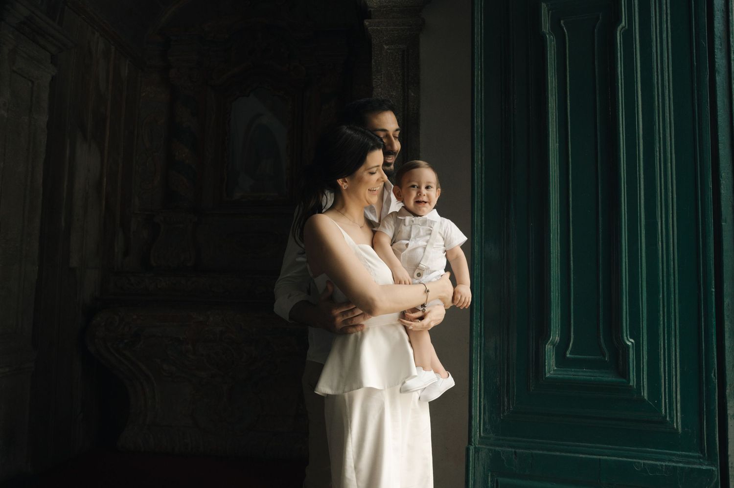 A wedding couple embraces in a romantic dance pose against an elegant dark green wall with ornate molding.